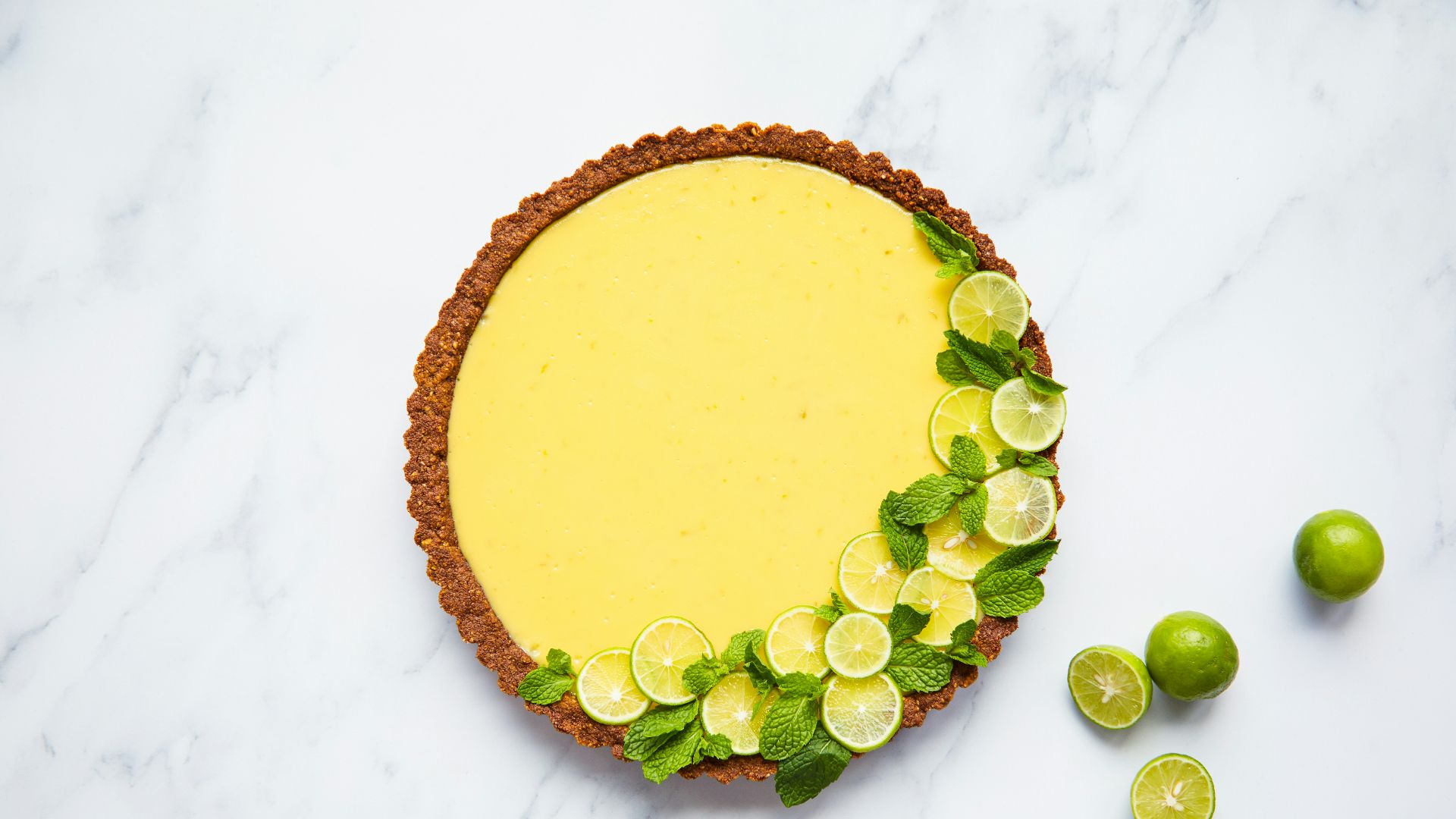 a pie with limes and lime slices on a marble surface