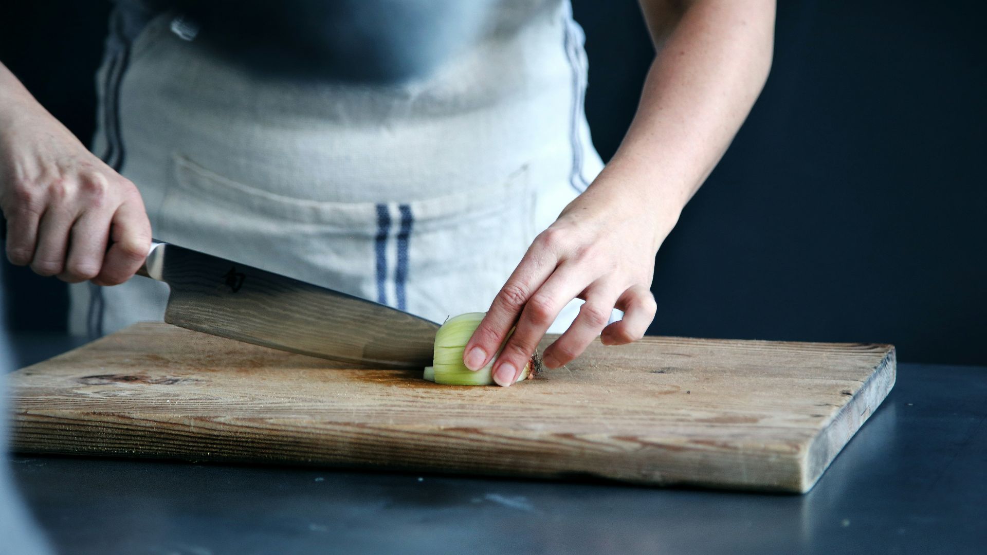 person slicing green vegetable on chopping board