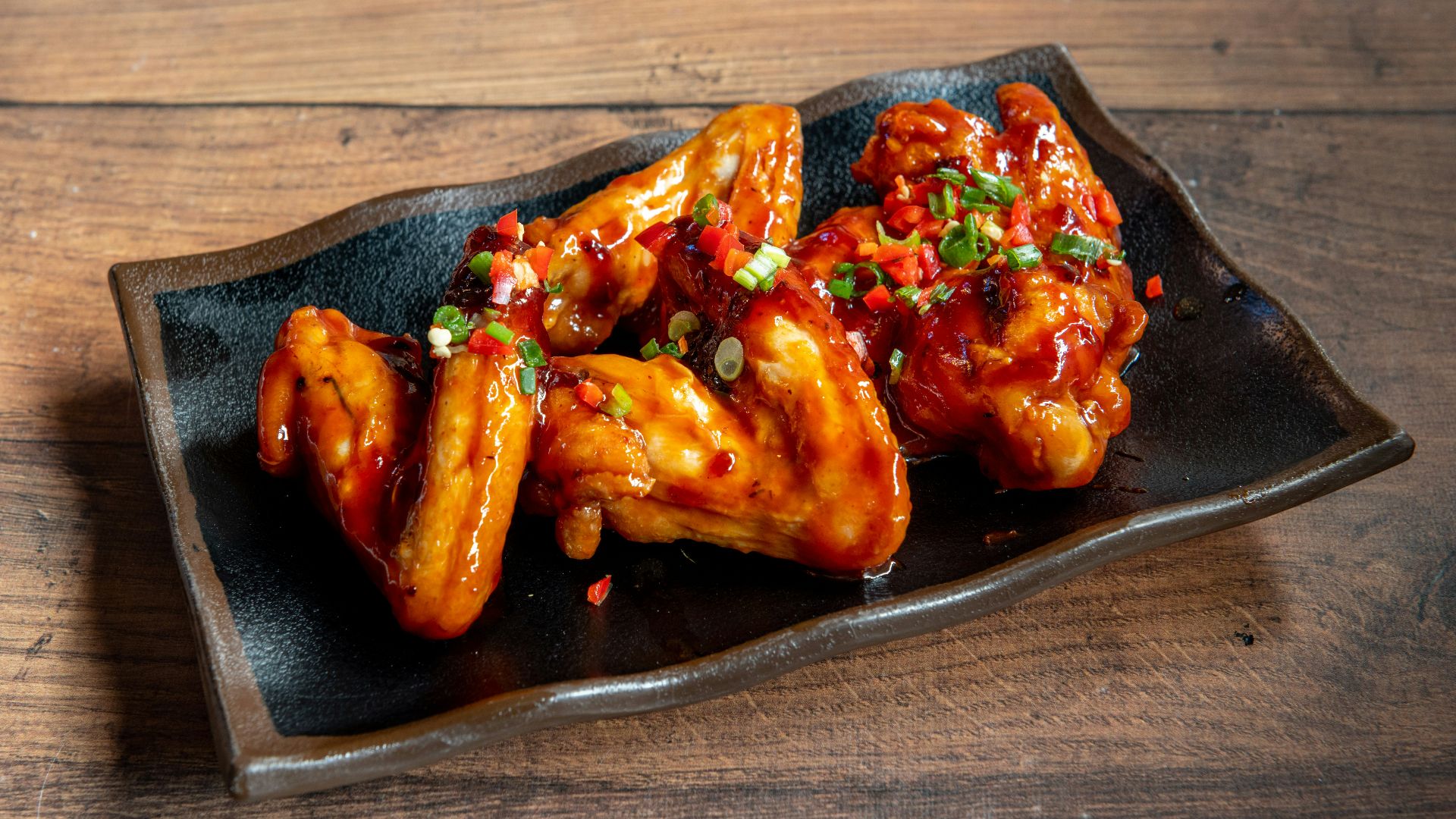 A black plate topped with wings covered in sauce