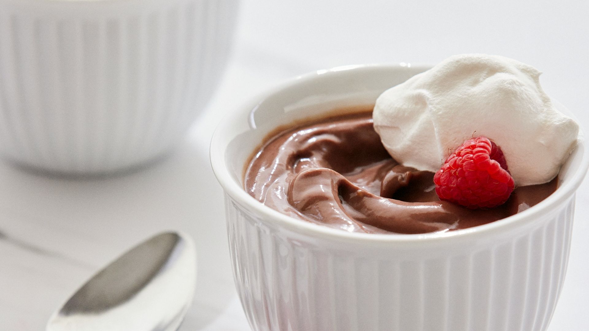 two bowls of chocolate pudding with raspberries on the side
