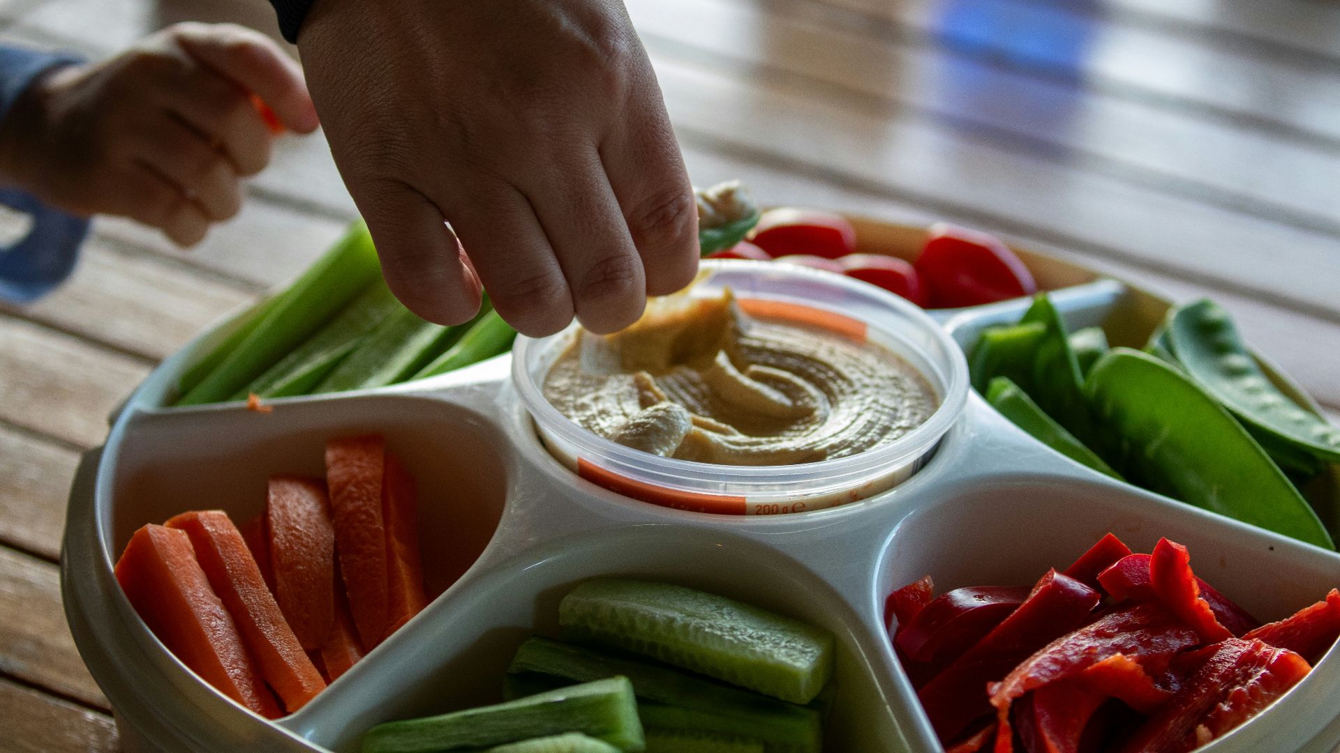 A person dipping dip into a bowl of vegetables
