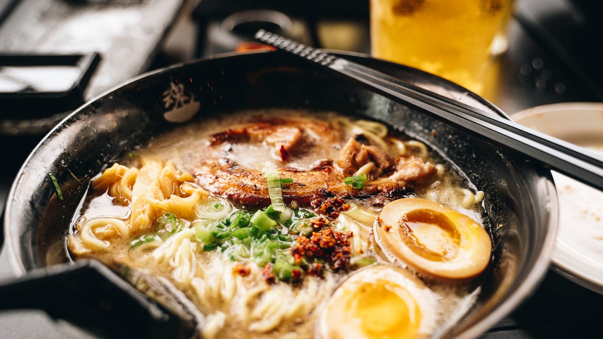 a bowl of ramen with chopsticks and a glass of beer