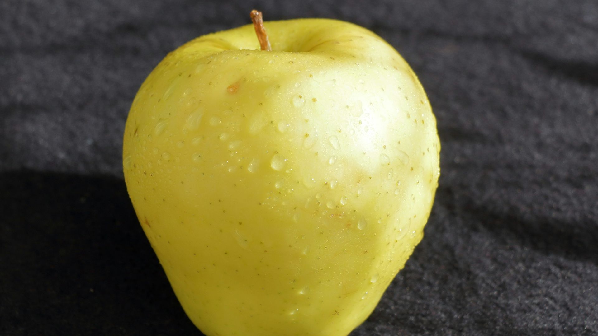 a yellow apple sitting on top of a black surface