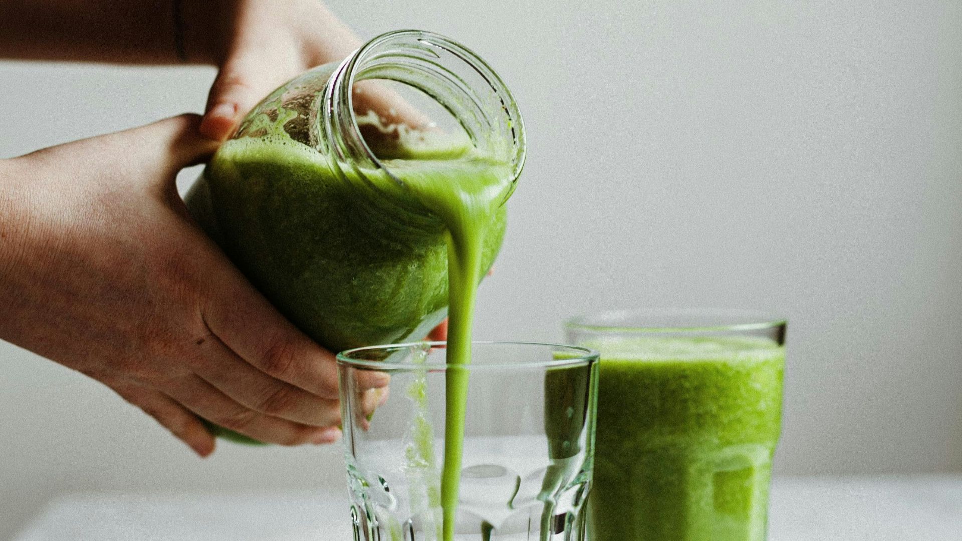 person holding clear drinking glass with green liquid