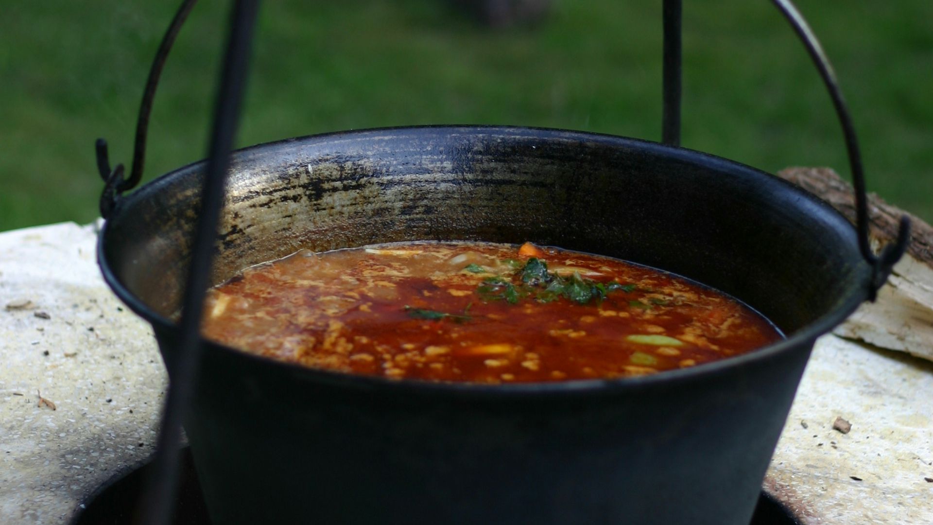 Soup is being cooked in a large hanging pot.