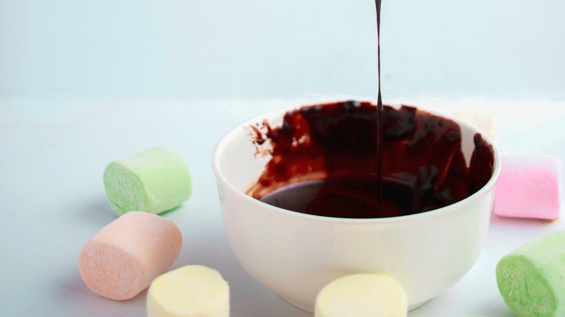 person dipping marshmallow in chocolate syrup