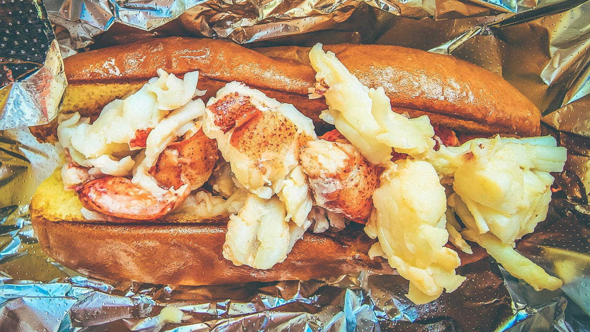 a hot dog with shrimp and potatoes on a piece of tin foil