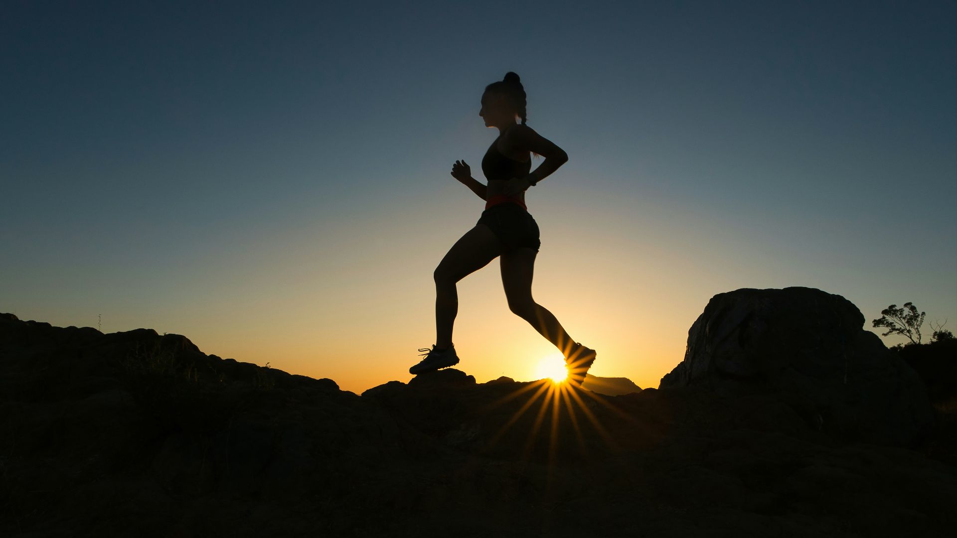 silhouette of man jumping on rocky mountain during sunset