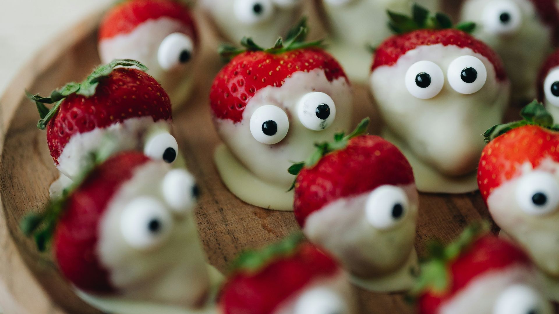 a wooden plate topped with strawberries covered in googly eyes