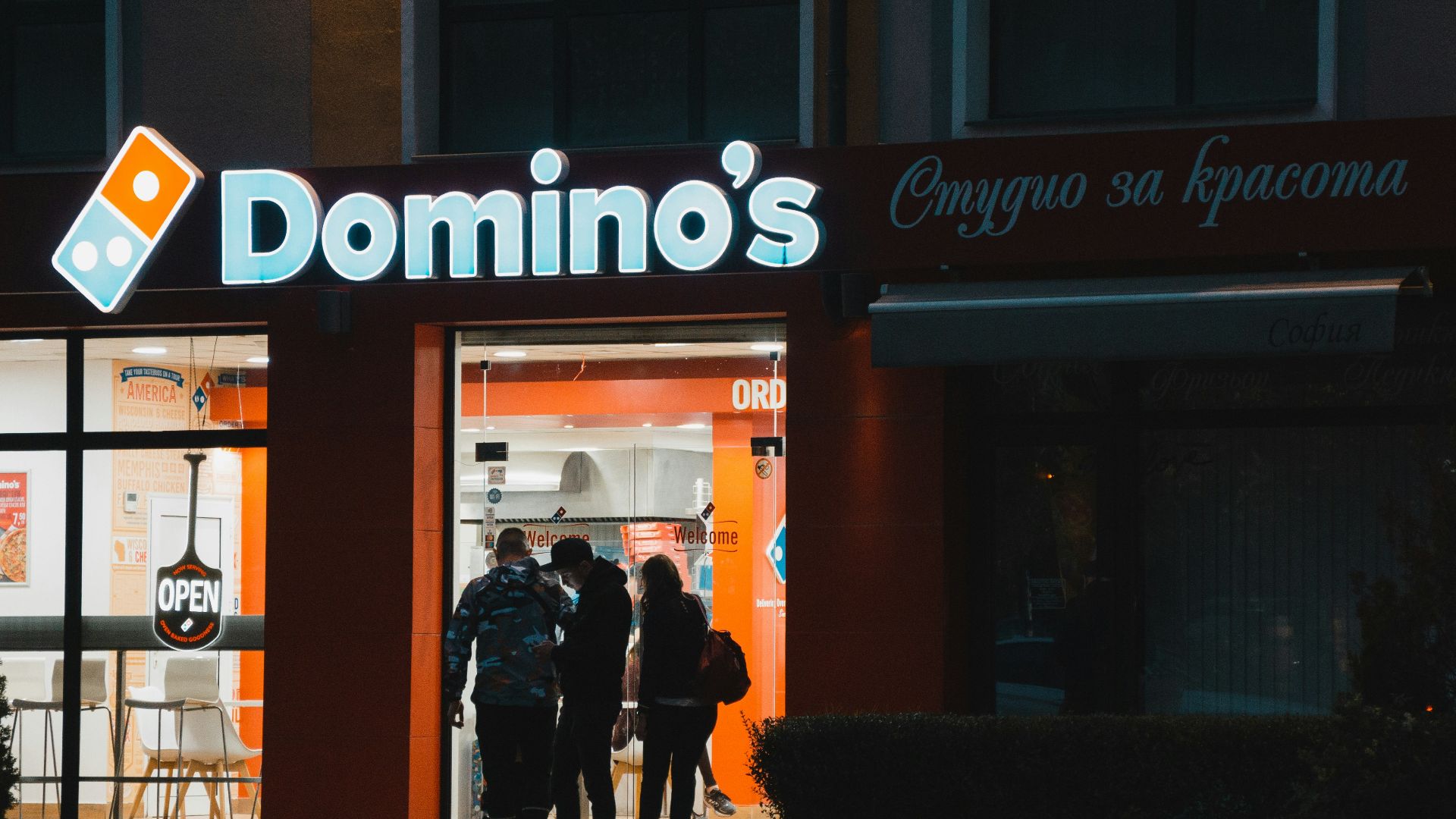 a group of people standing outside of a domino's store