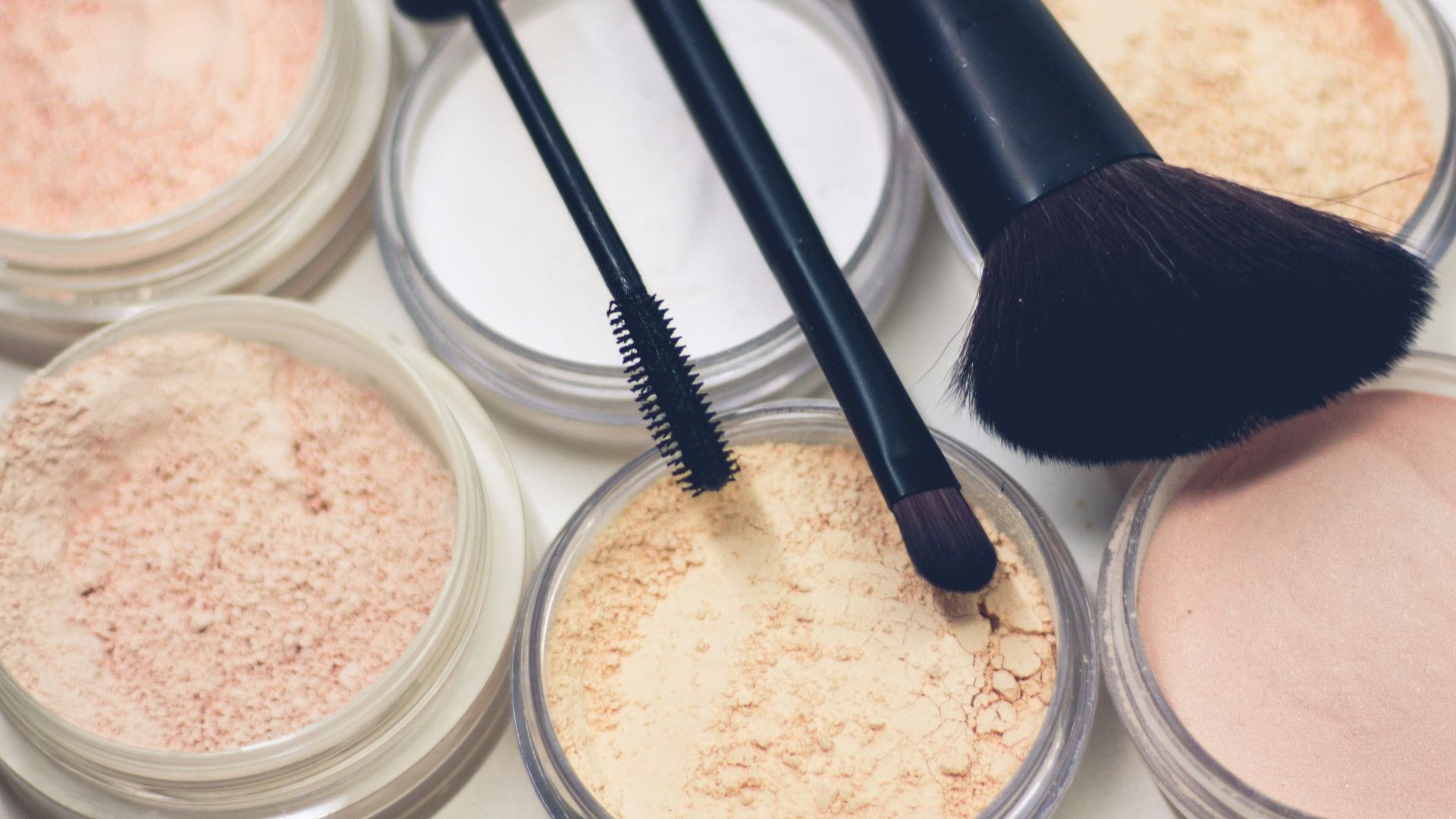 three makeup brushes on top of compact powders