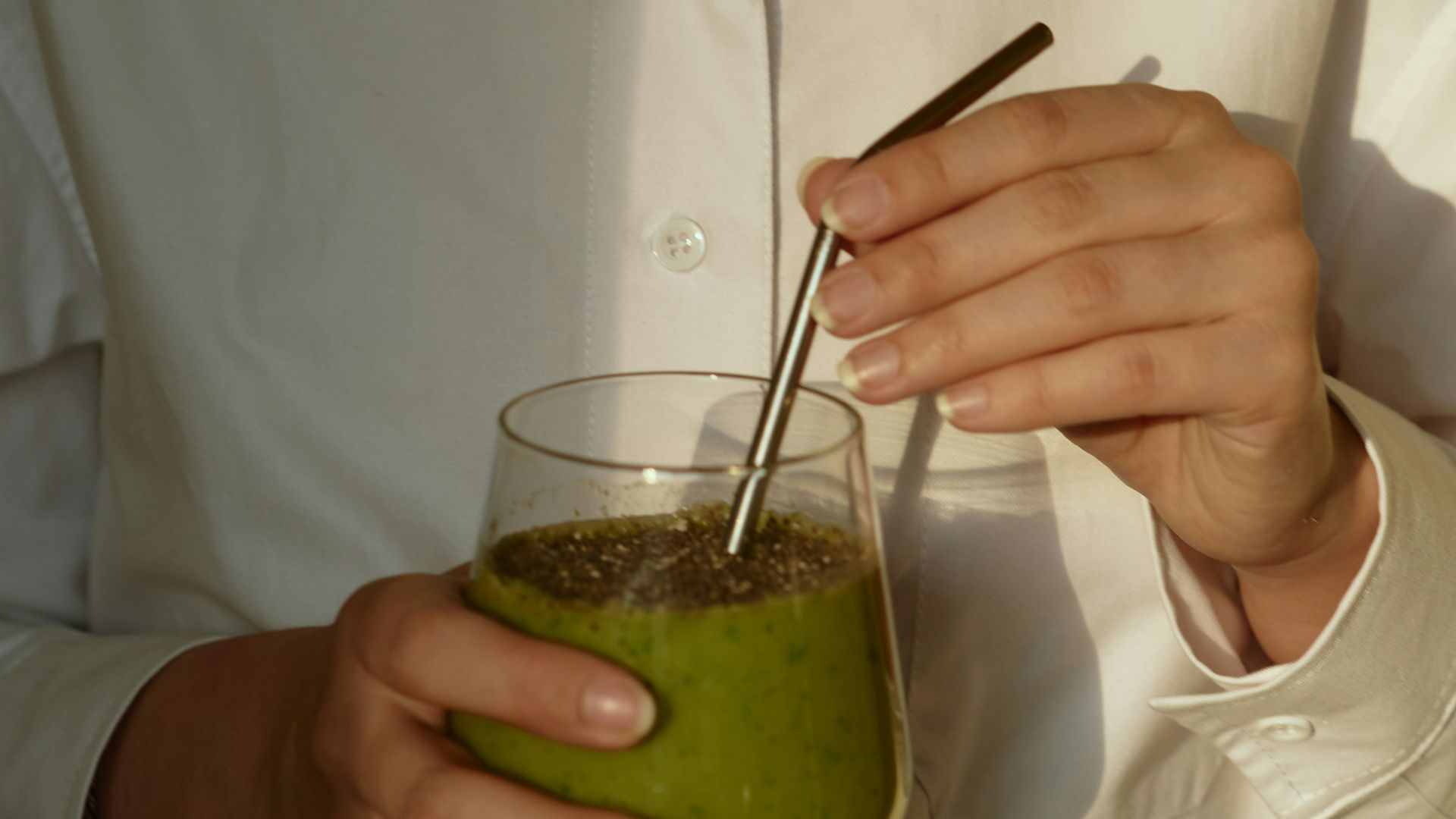 person in white button up shirt holding clear drinking glass with green liquid