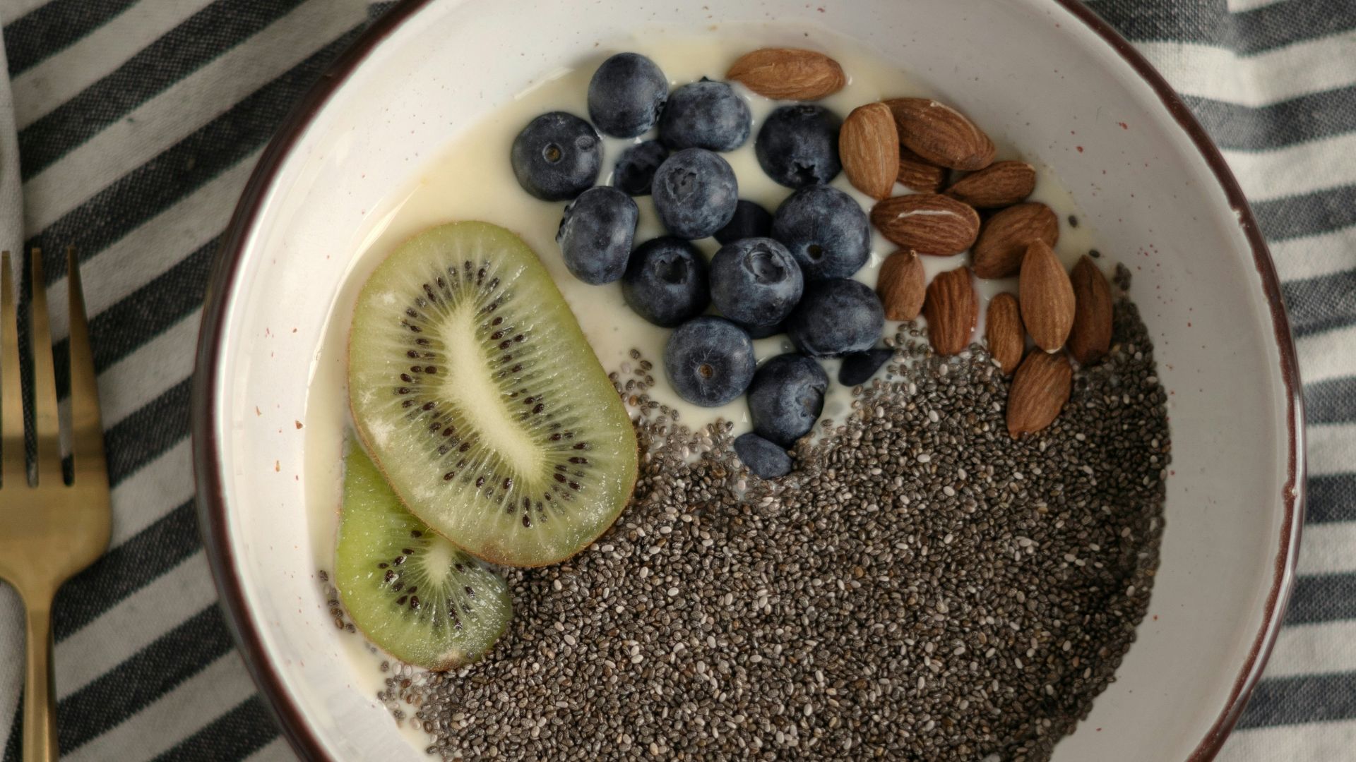a bowl of cereal with kiwis, bananas, and blueberries