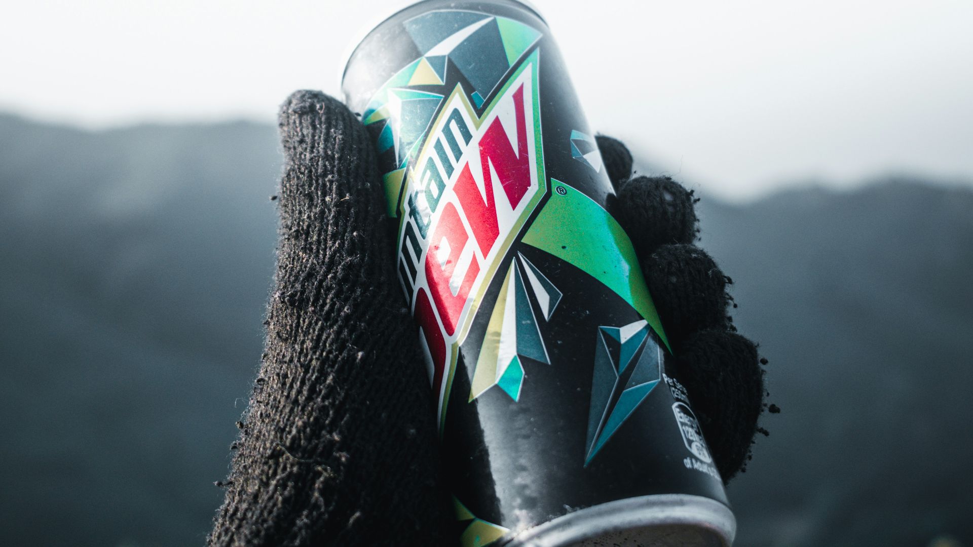 a hand holding a can of wnc on top of a mountain