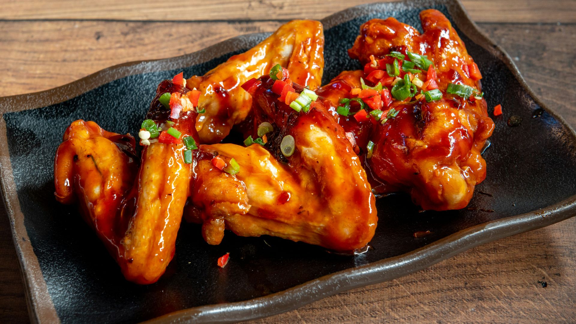 A black plate topped with wings covered in sauce