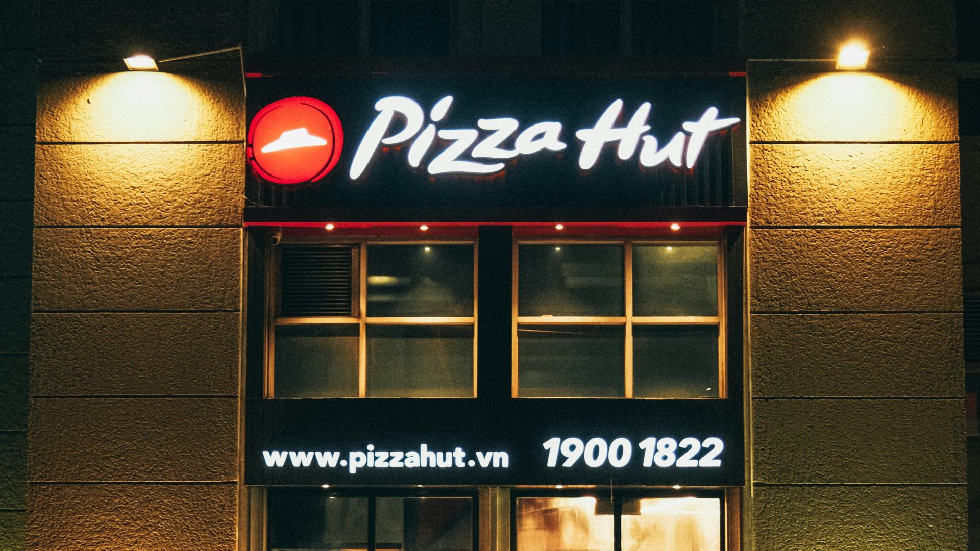 a man walking past a pizza hut at night