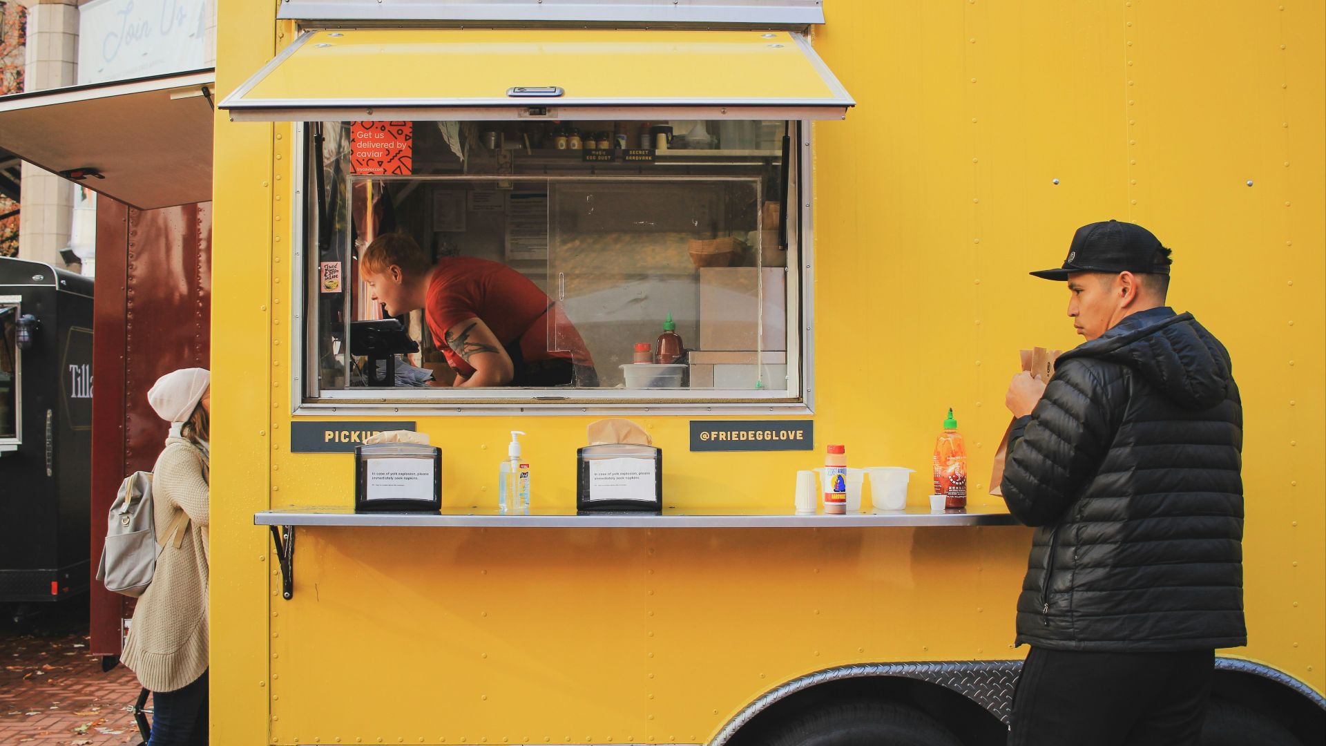 man in black hooded bubble jacket standing outside of food stall