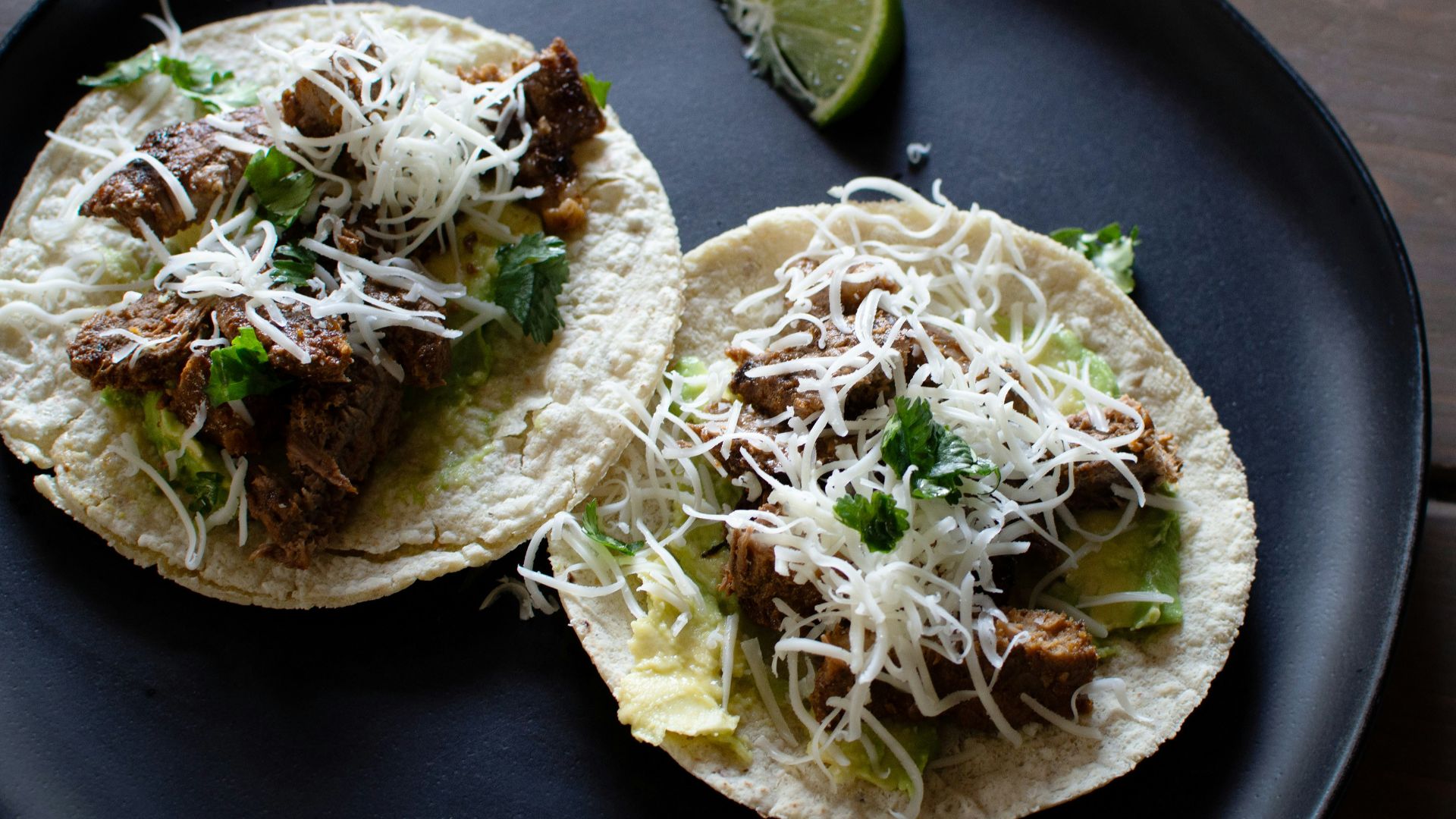 two tacos on a plate with a lime wedge