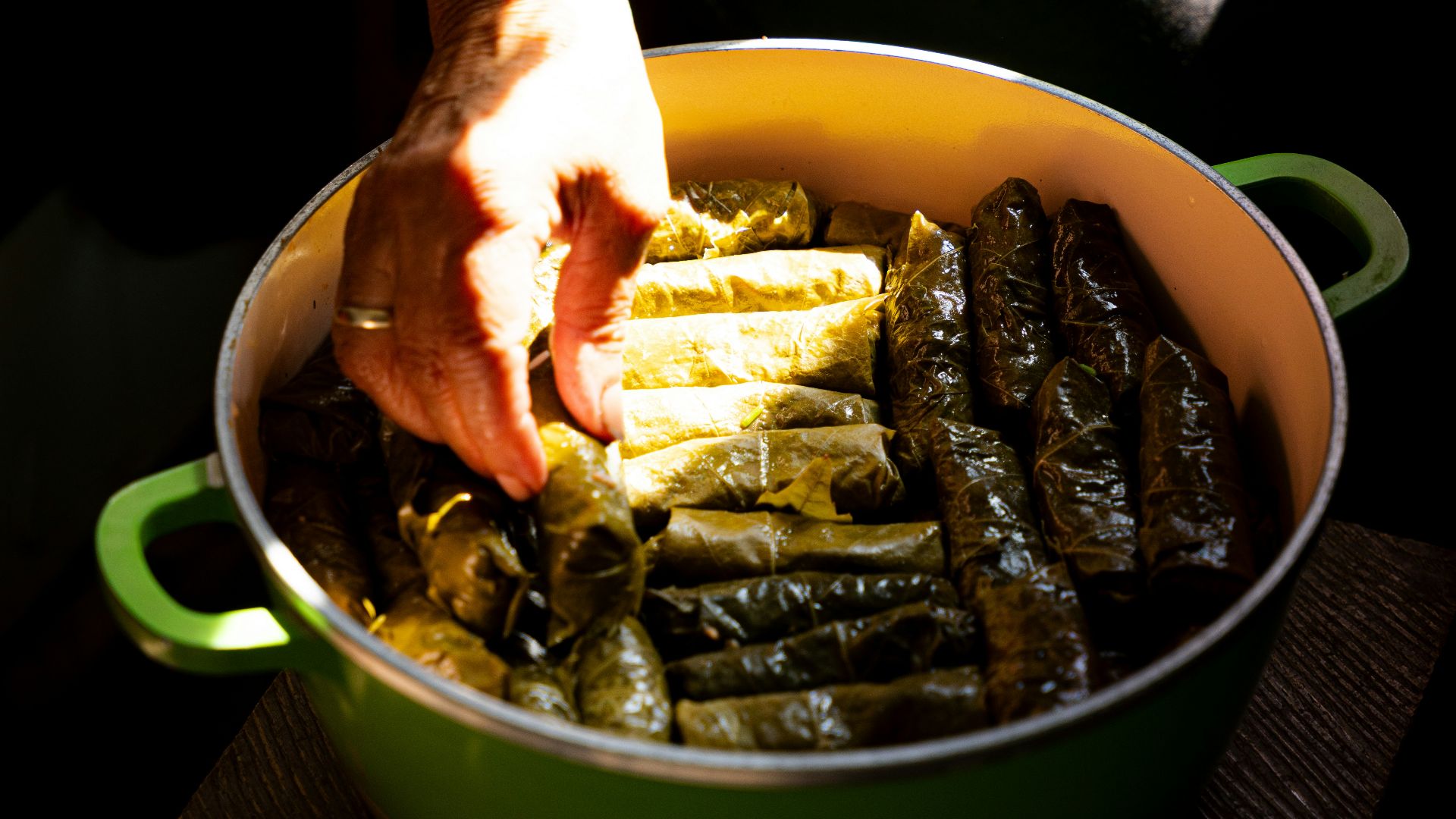 Hands arranging stuffed grape leaves in a pot.