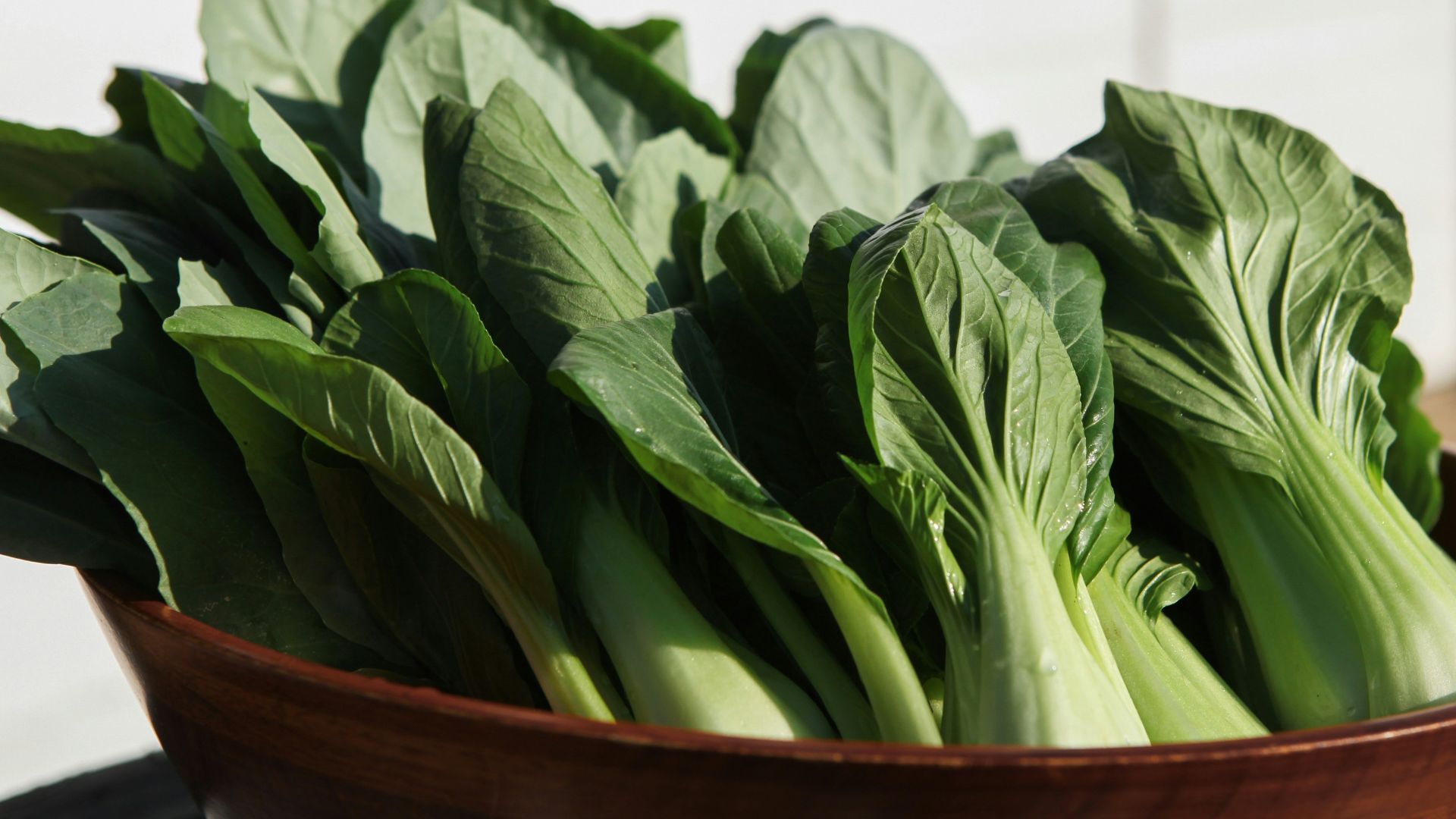 a wooden bowl filled with green leafy vegetables