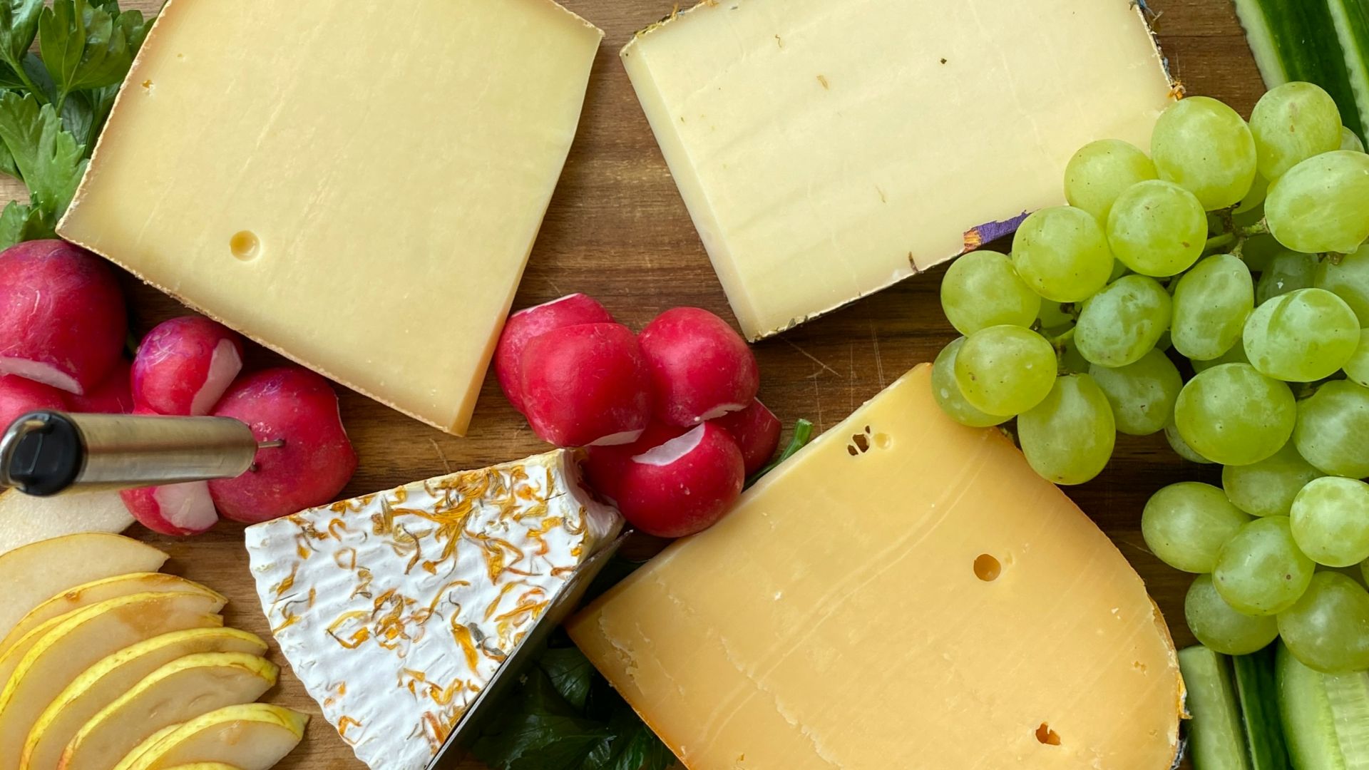 a wooden cutting board topped with cheese and fruit