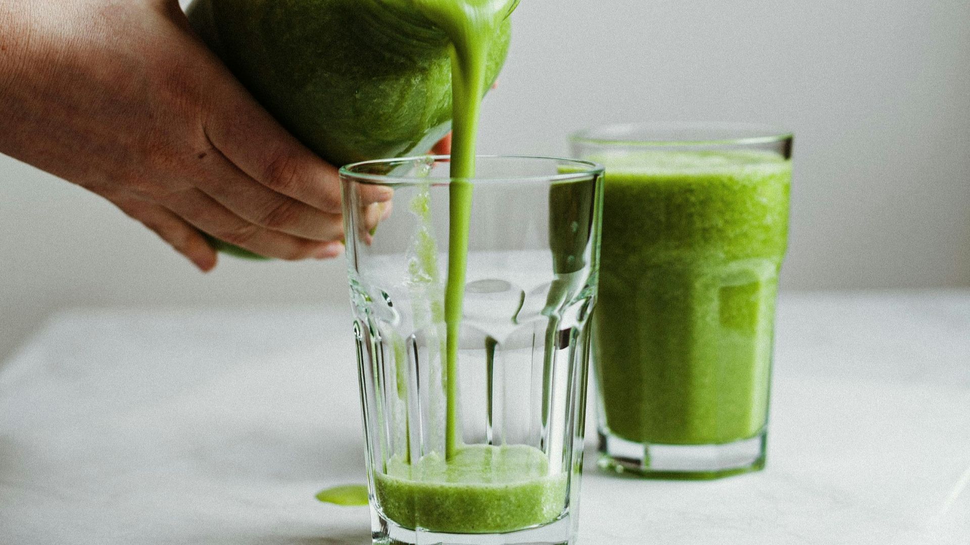 person holding clear drinking glass with green liquid