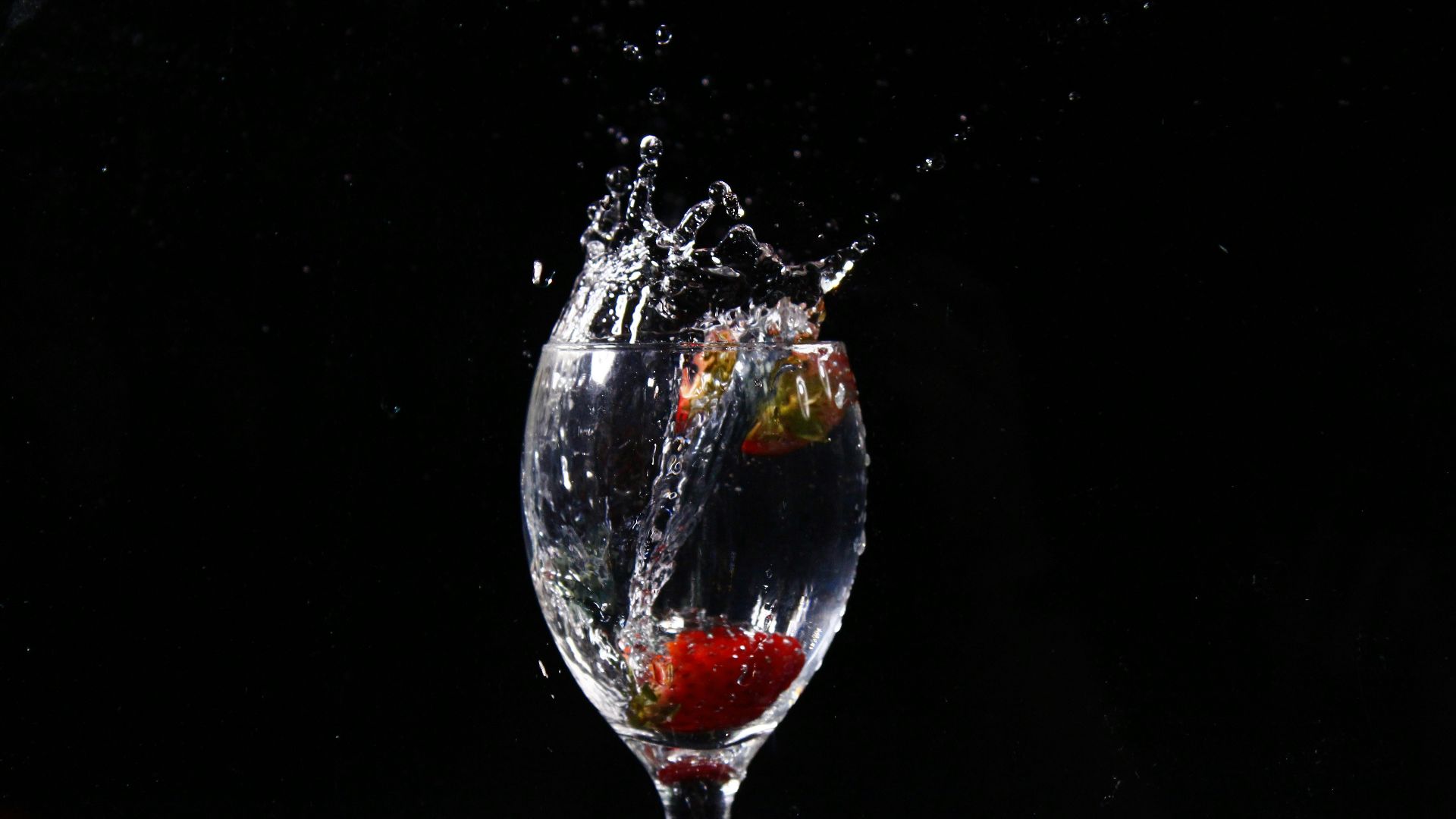 a glass of water with a strawberry splashing out of it