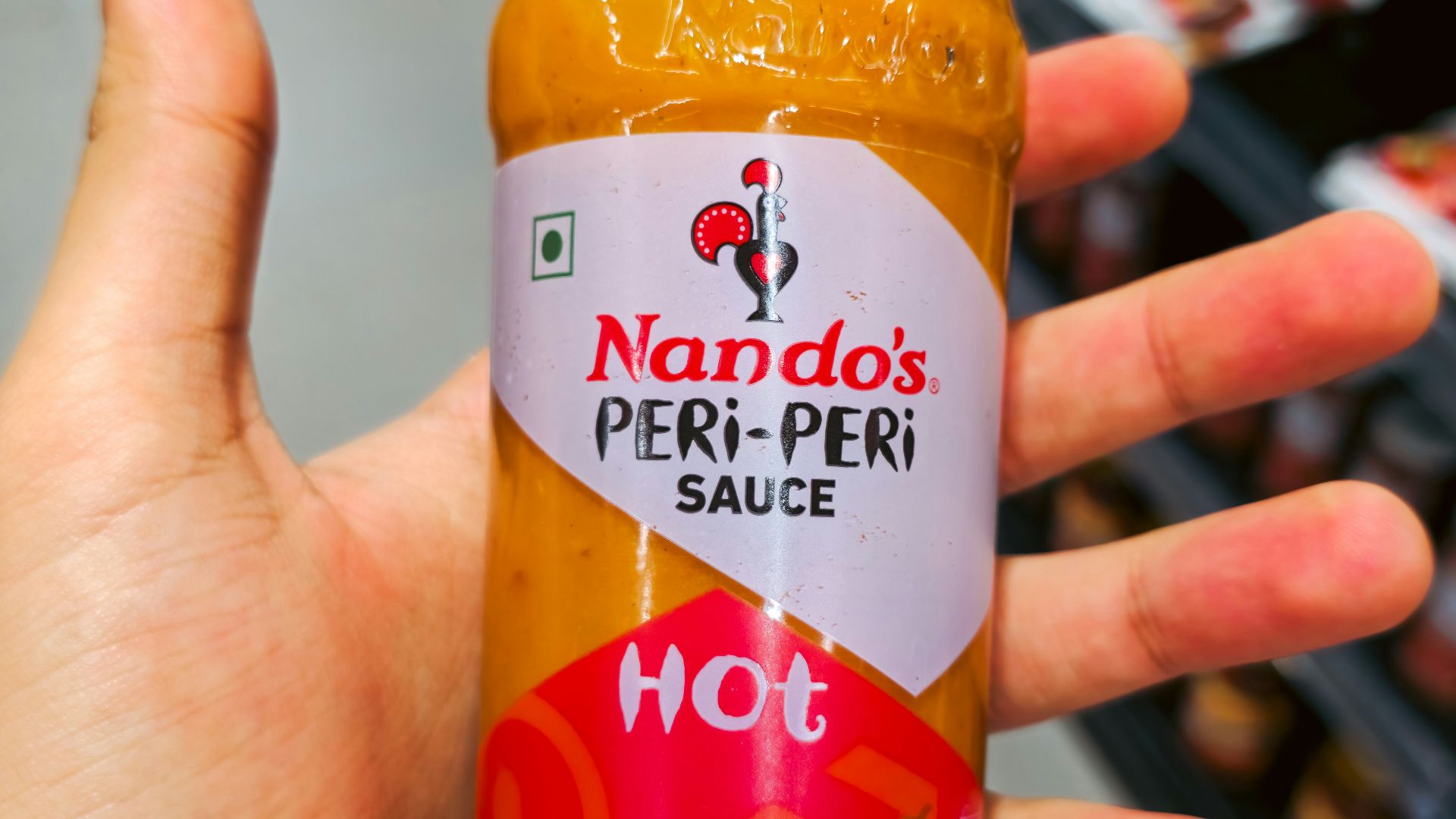 Hand holding a bottle of nando's peri-peri hot sauce