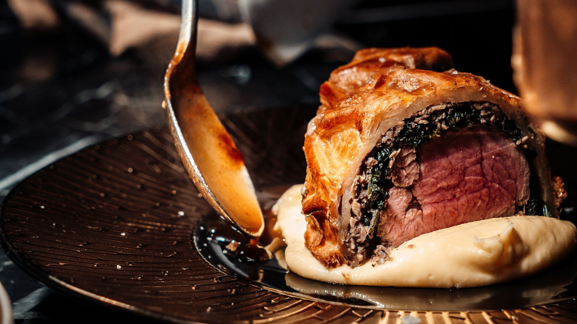 person holding stainless steel fork and knife slicing meat on black ceramic plate