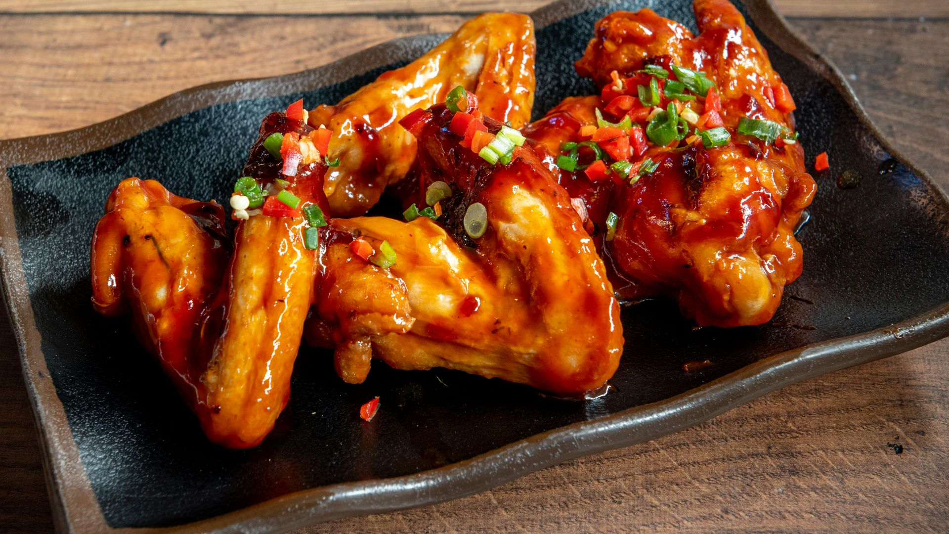 A black plate topped with wings covered in sauce