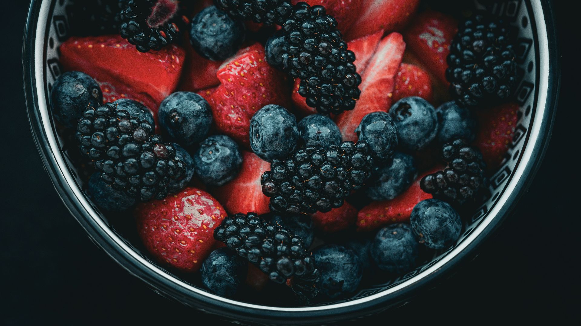 a bowl of berries and strawberries on a black background