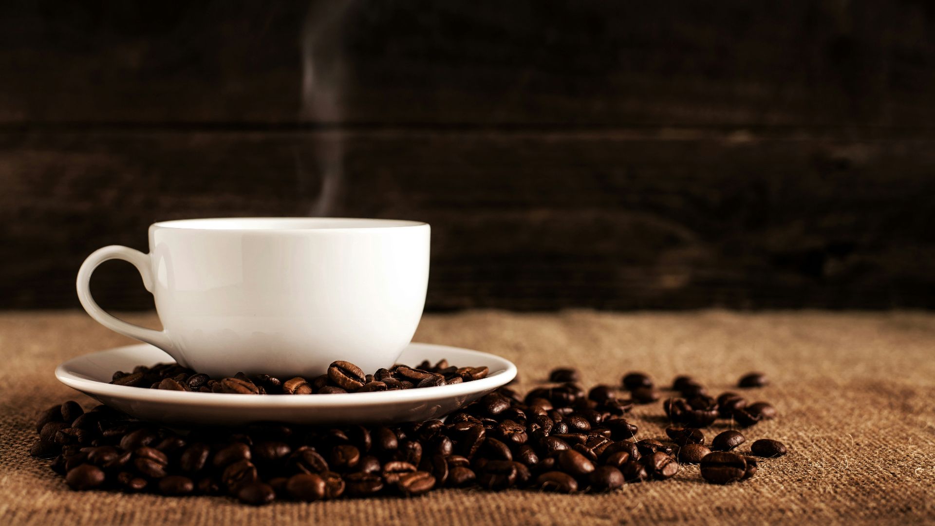 white ceramic mug and saucer with coffee beans on brown textile