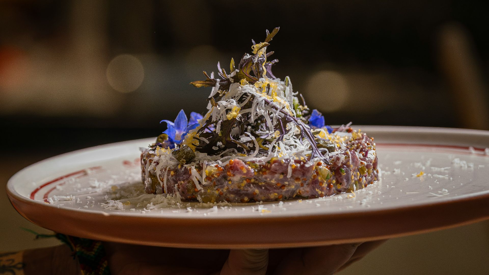 Gourmet beef tartare dish garnished with herbs and flowers.