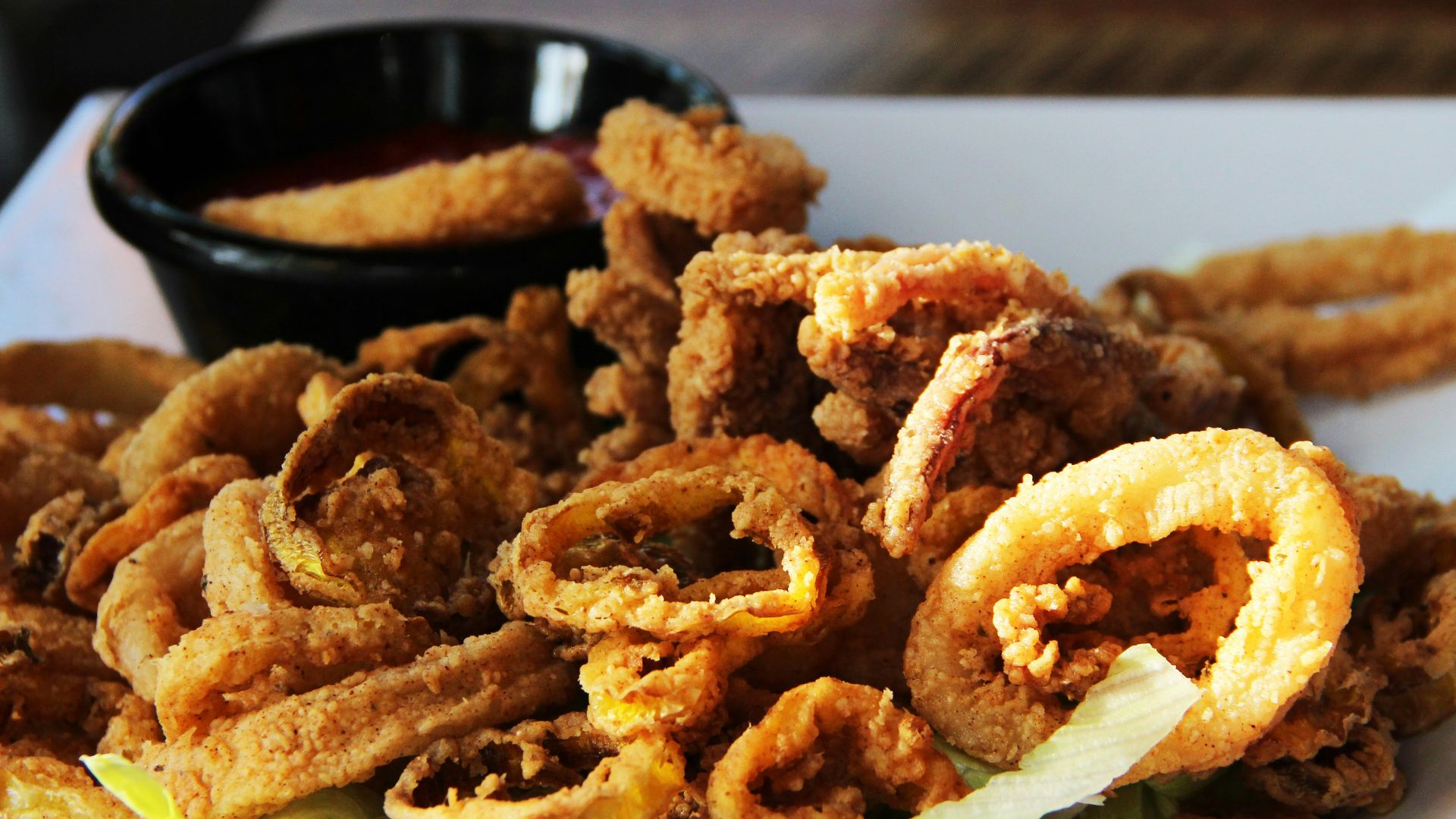 a white plate topped with onion rings and a bowl of dipping sauce