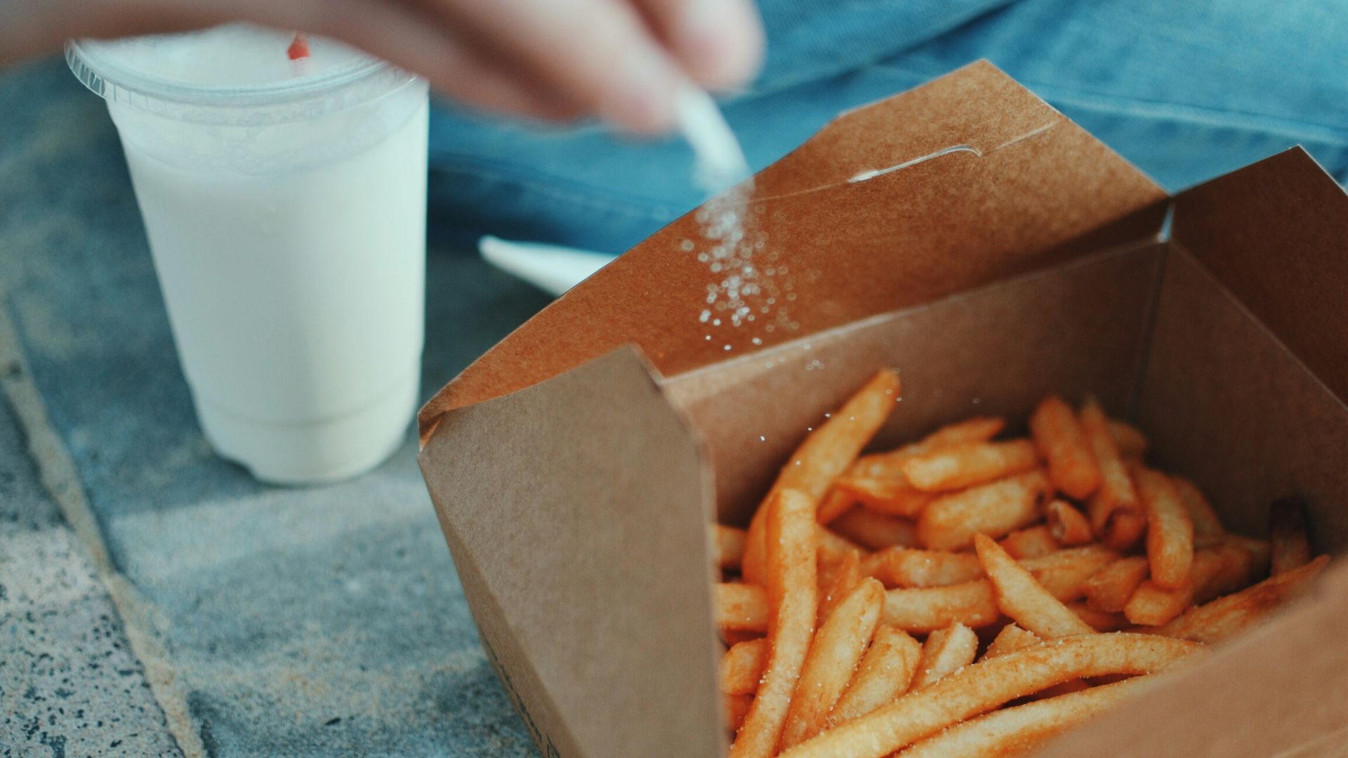 person sprinkling salt in fries