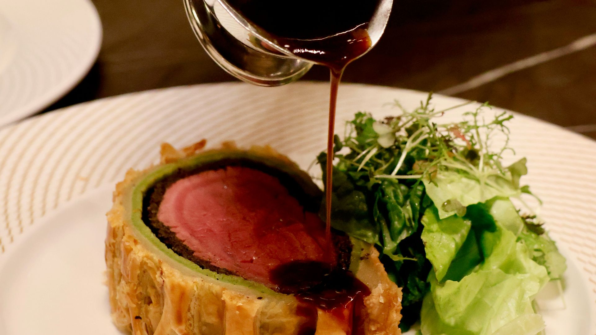 a person pouring sauce on a piece of meat