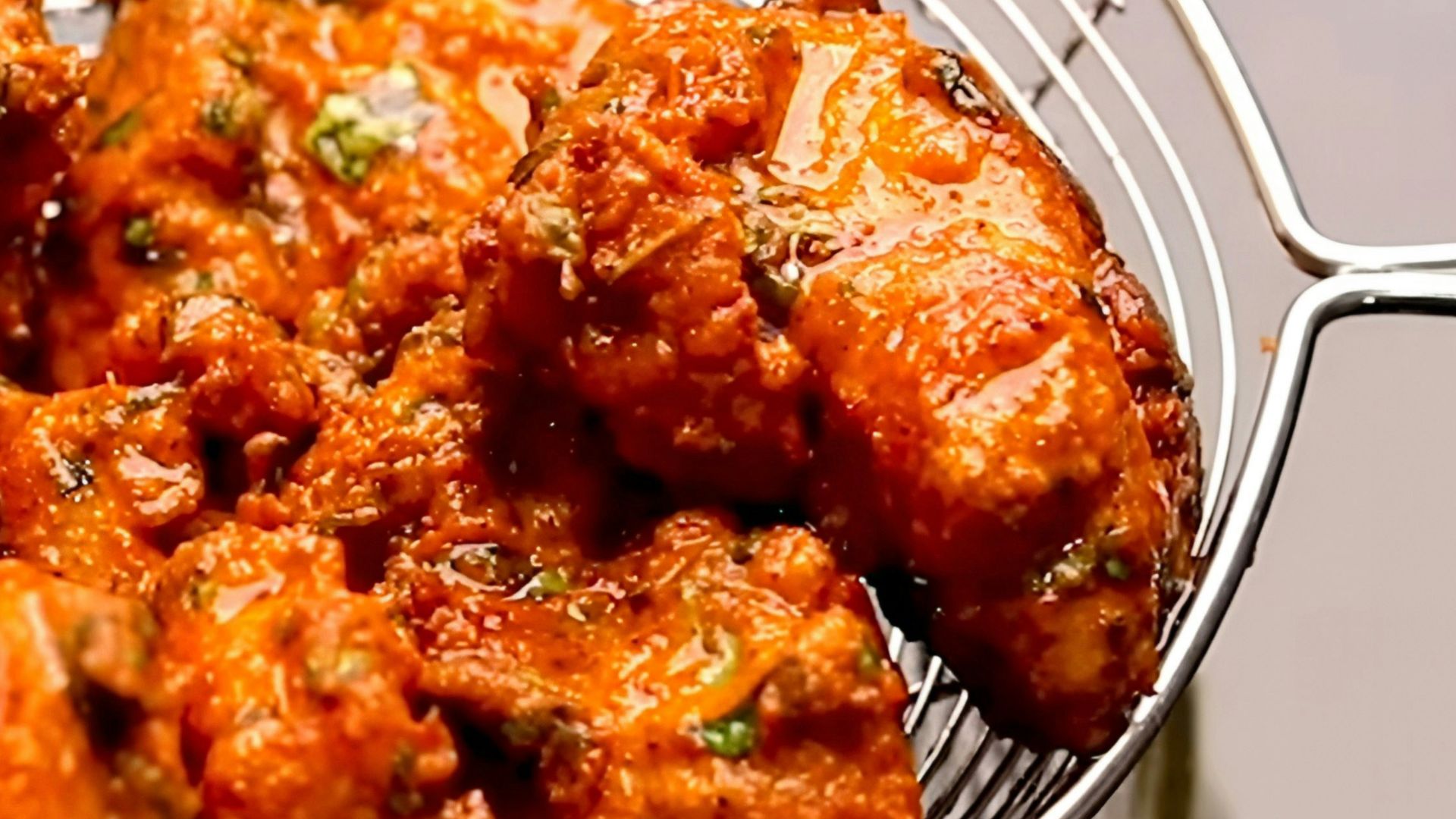 Crispy pakoras being drained in a metal strainer.