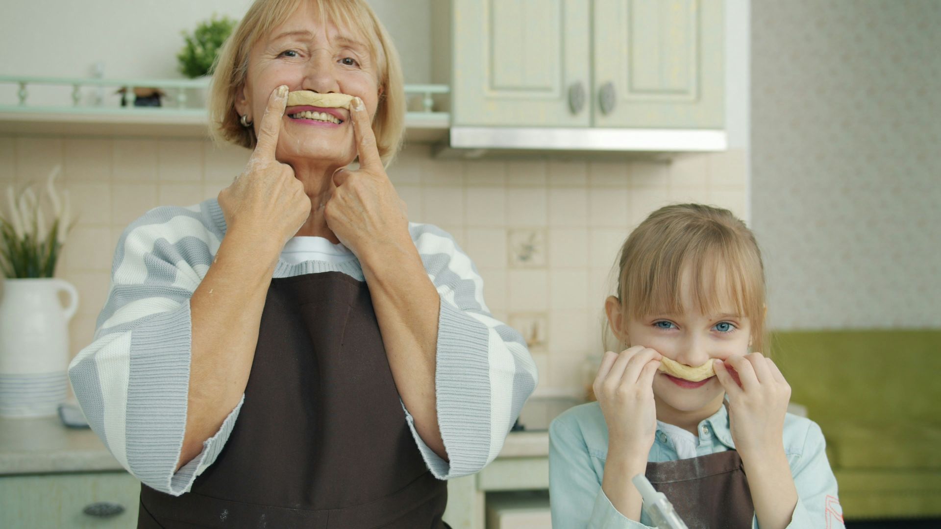 Grandmother and granddaughter making mustache shapes with food.