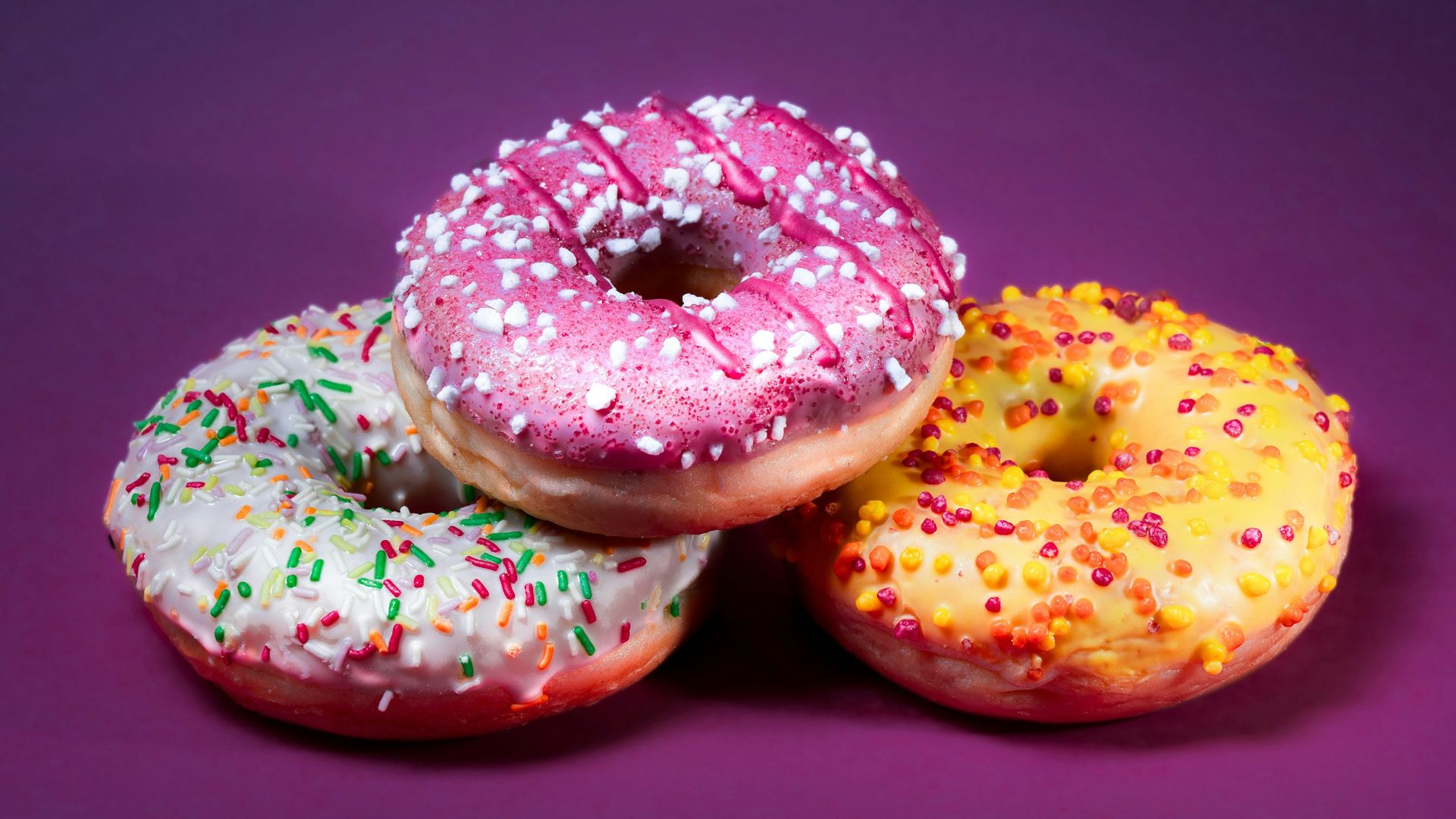 three donuts with sprinkles on a purple background