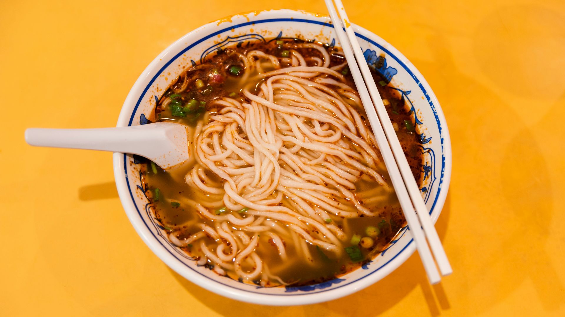 white and blue ceramic bowl with noodles and chopsticks