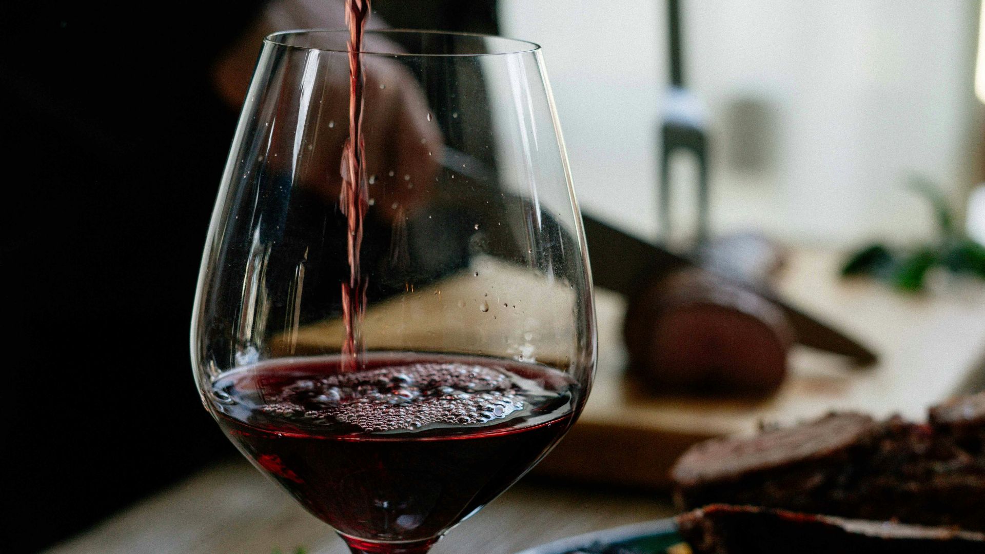 person pouring red wine on wine glass