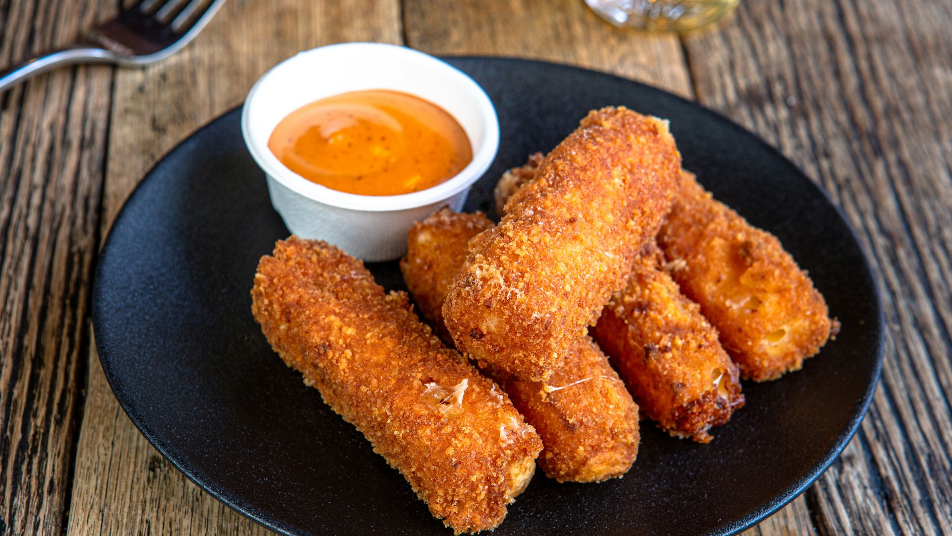 A black plate topped with fried food next to a cup of dipping sauce