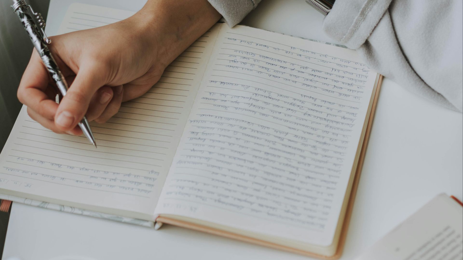 person writing on notebook beside mug