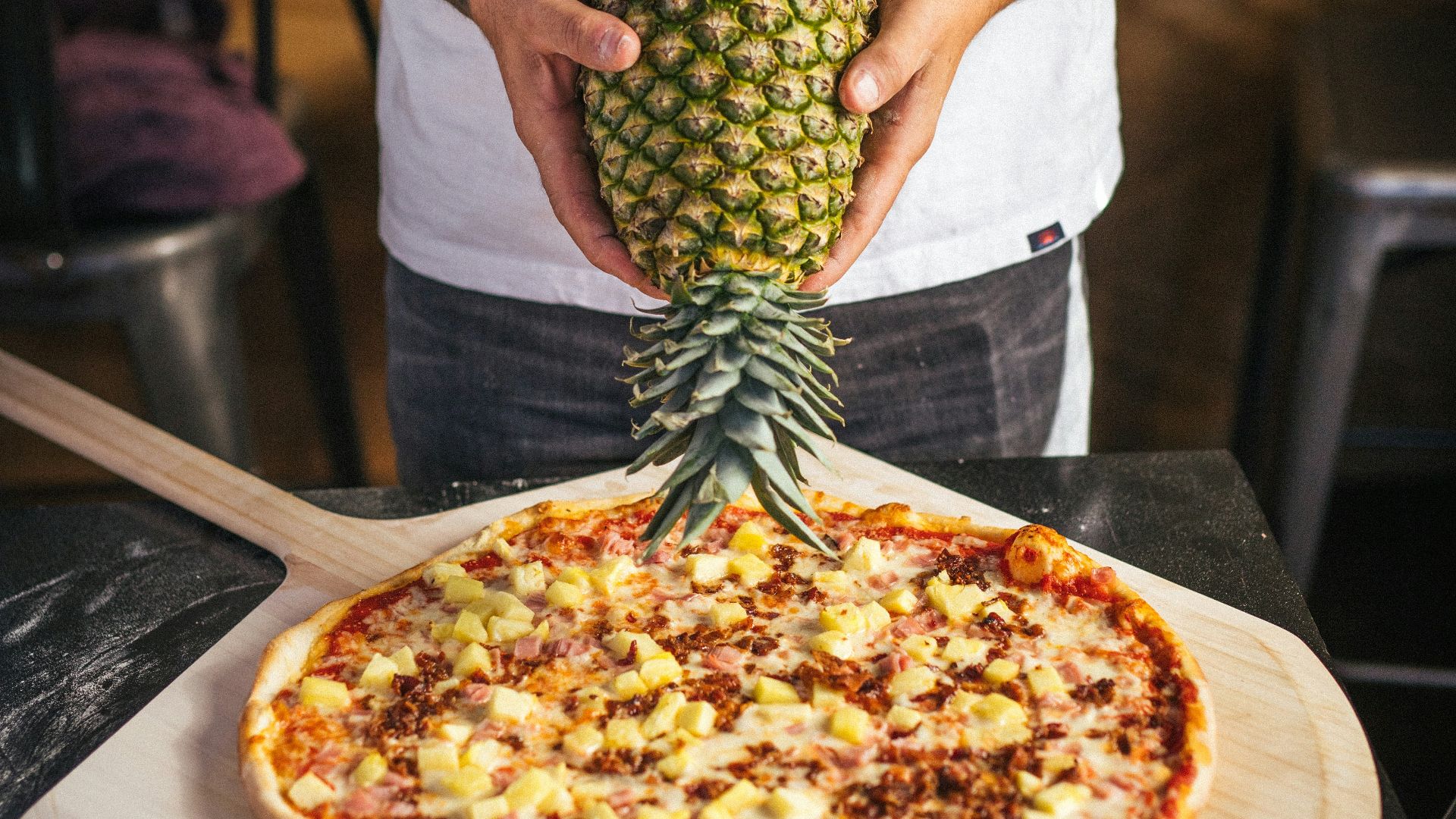 a man holding a pineapple on top of a pizza