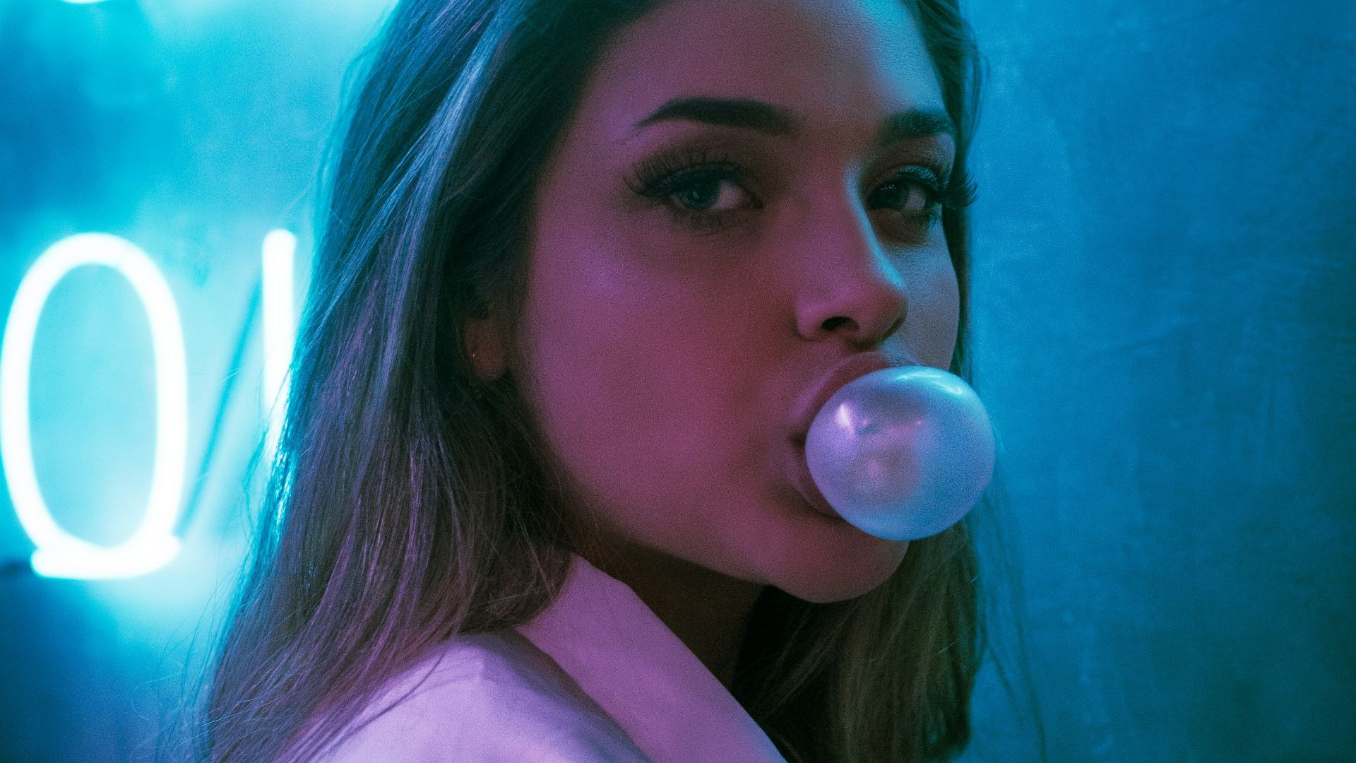 selective focus photo of woman blowing gum standing in front of turned-on neon signage