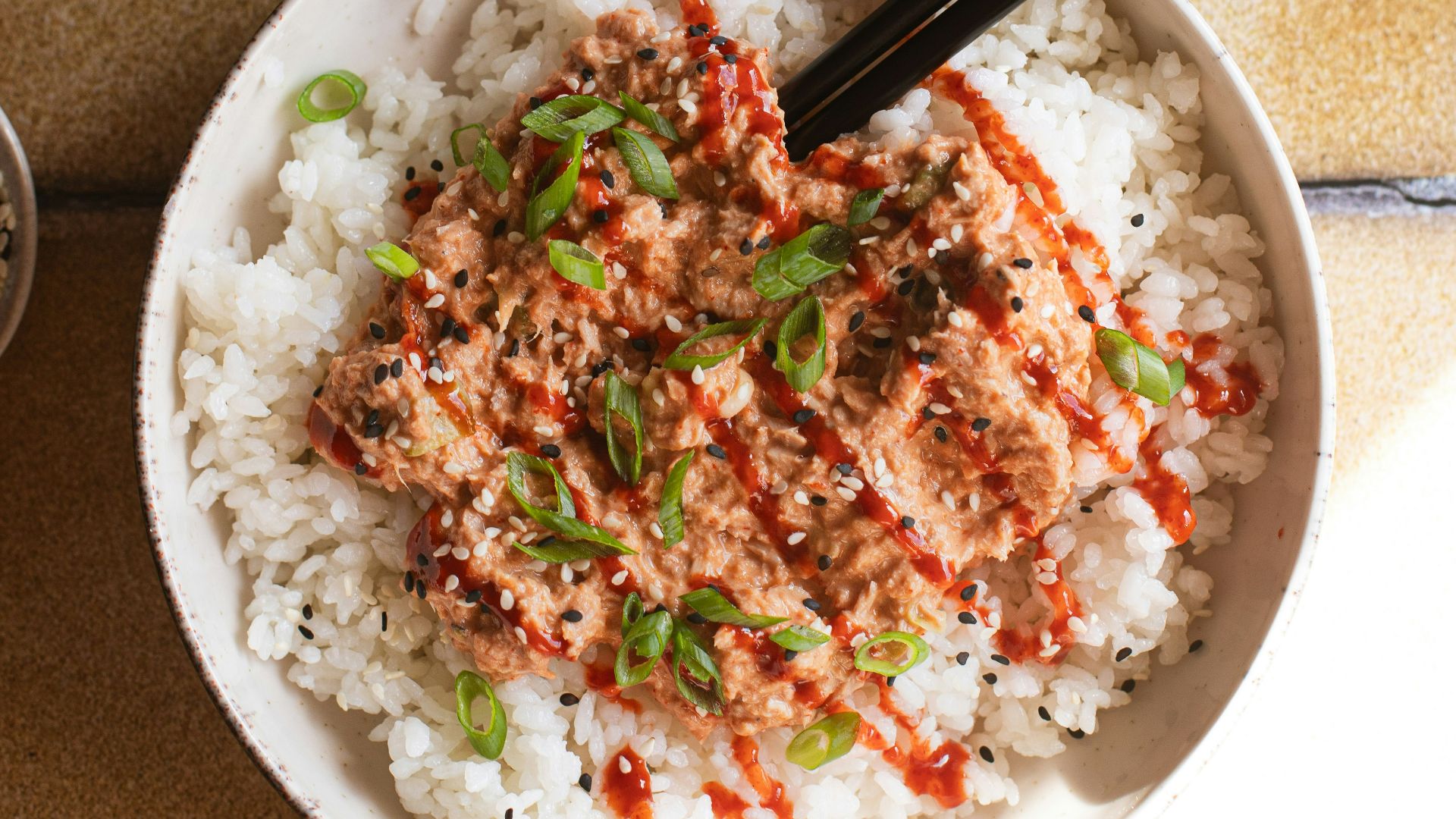 a bowl of rice with chopsticks and a plate of sushi