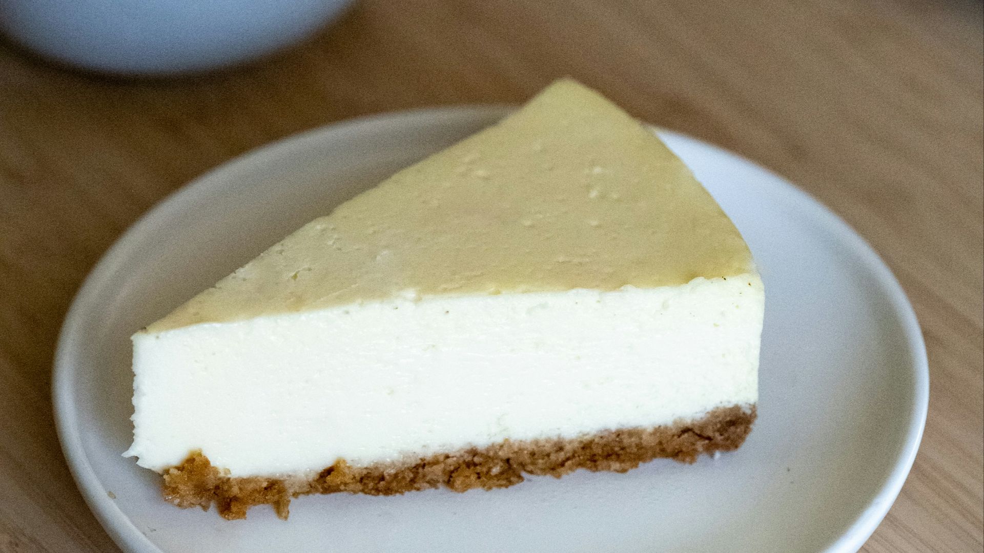 a piece of cheesecake on a plate next to a cup of tea