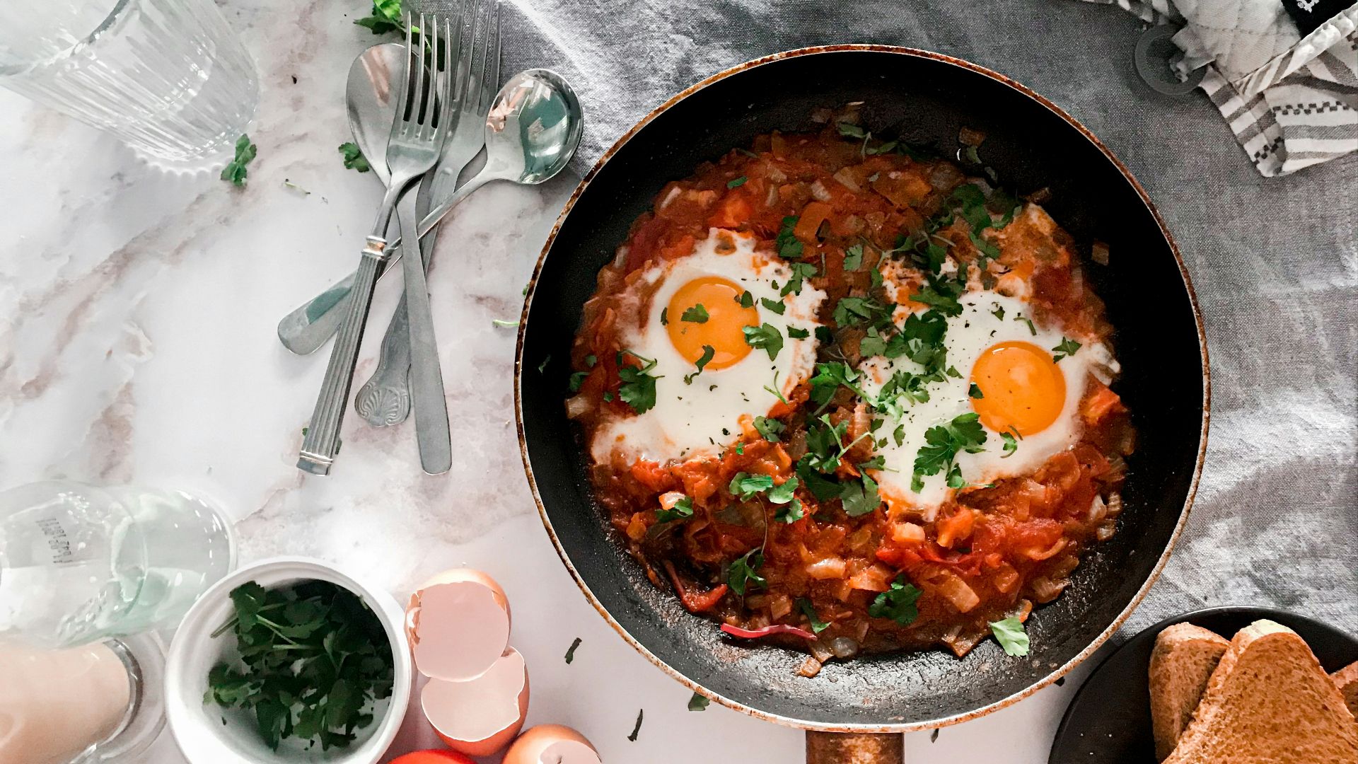 tomato soup on black cooking pan beside stainless steel fork and bread knife