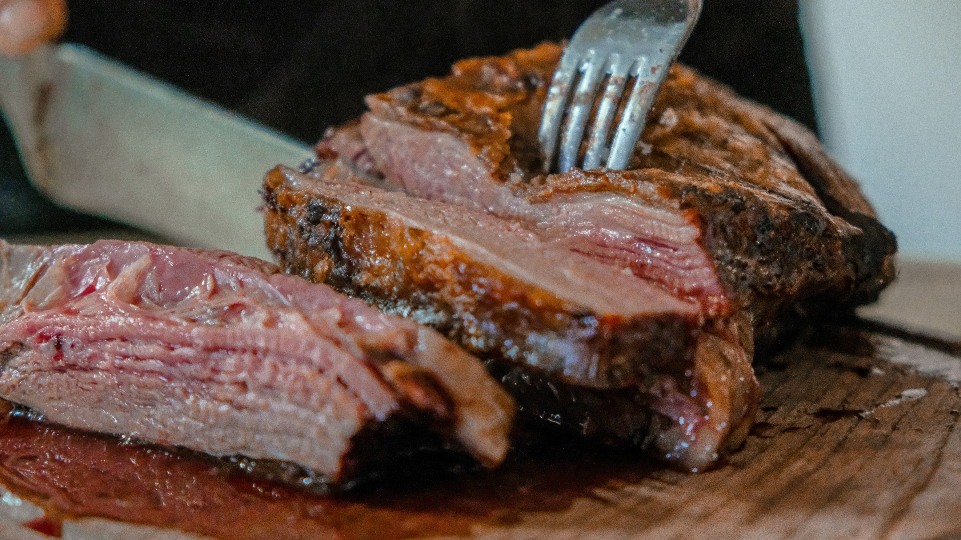 person slicing a meat on brown wooden board