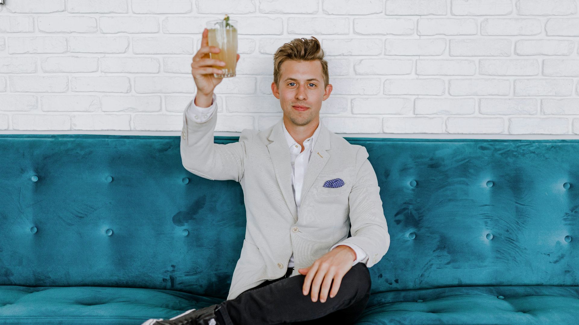 man in gray blazer raising drinking glass while sitting on sofa